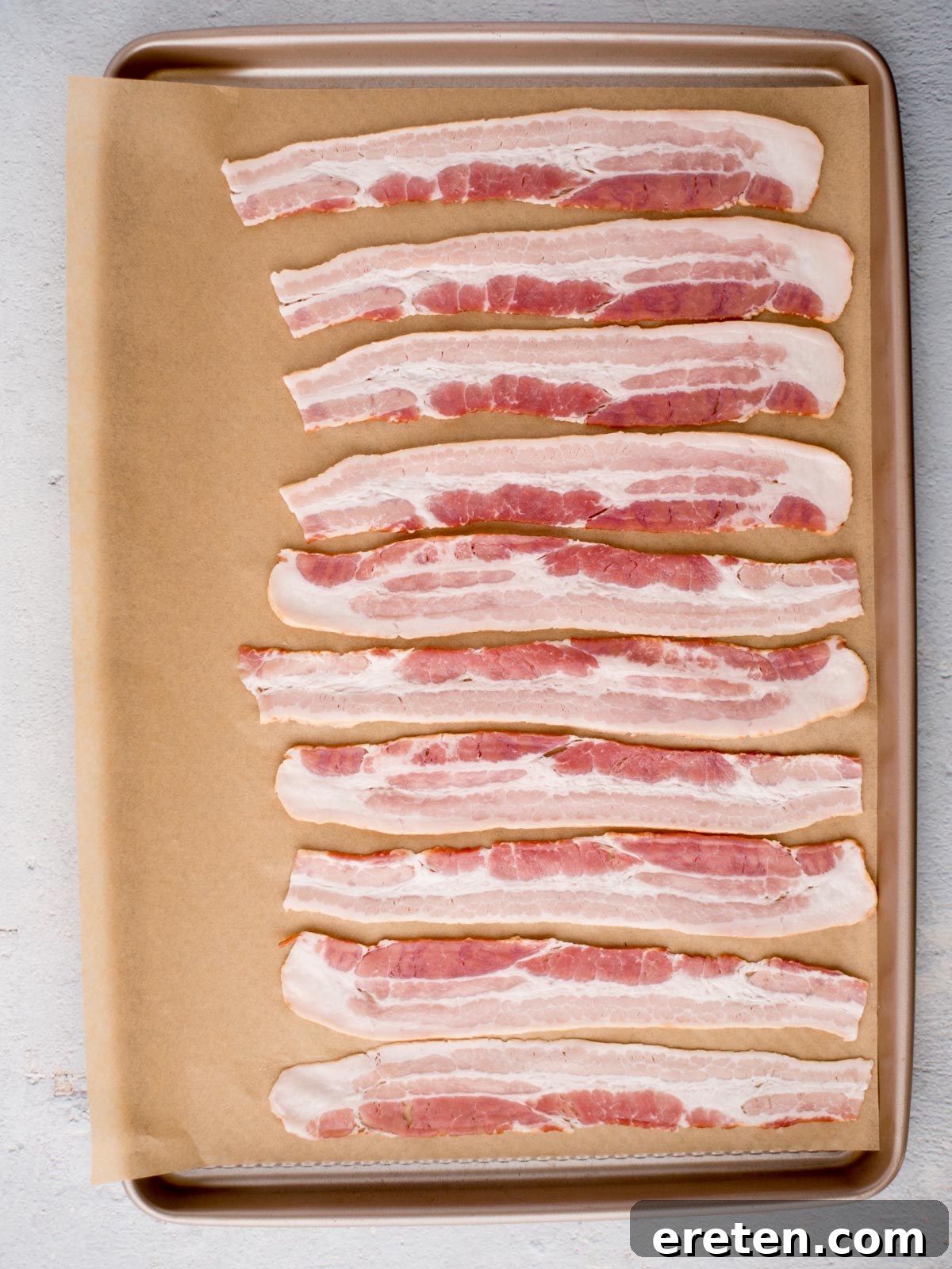 Golden Nectar Bacon 4 Raw bacon placed in strips on a parchment paper covered baking sheet to prepare honey bacon.