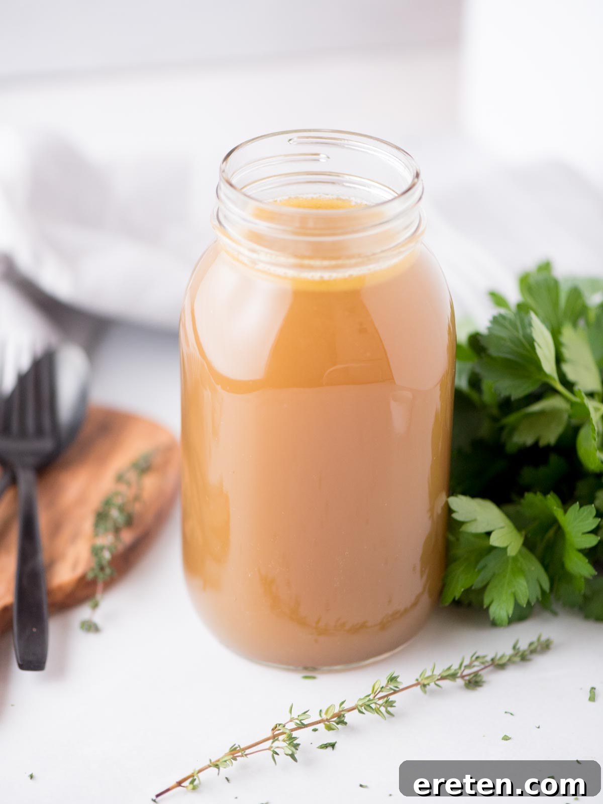 The Ultimate Homemade Chicken Broth 2 Homemade chicken broth in a mason jar, garnished with fresh thyme and parsley, set against a rustic background.