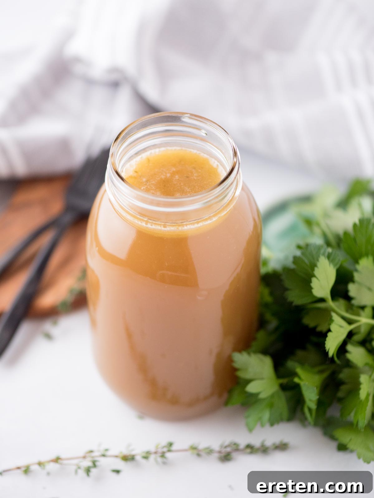 The Ultimate Homemade Chicken Broth 10 Homemade chicken broth in a mason jar, garnished with fresh thyme and parsley, set against a rustic background.