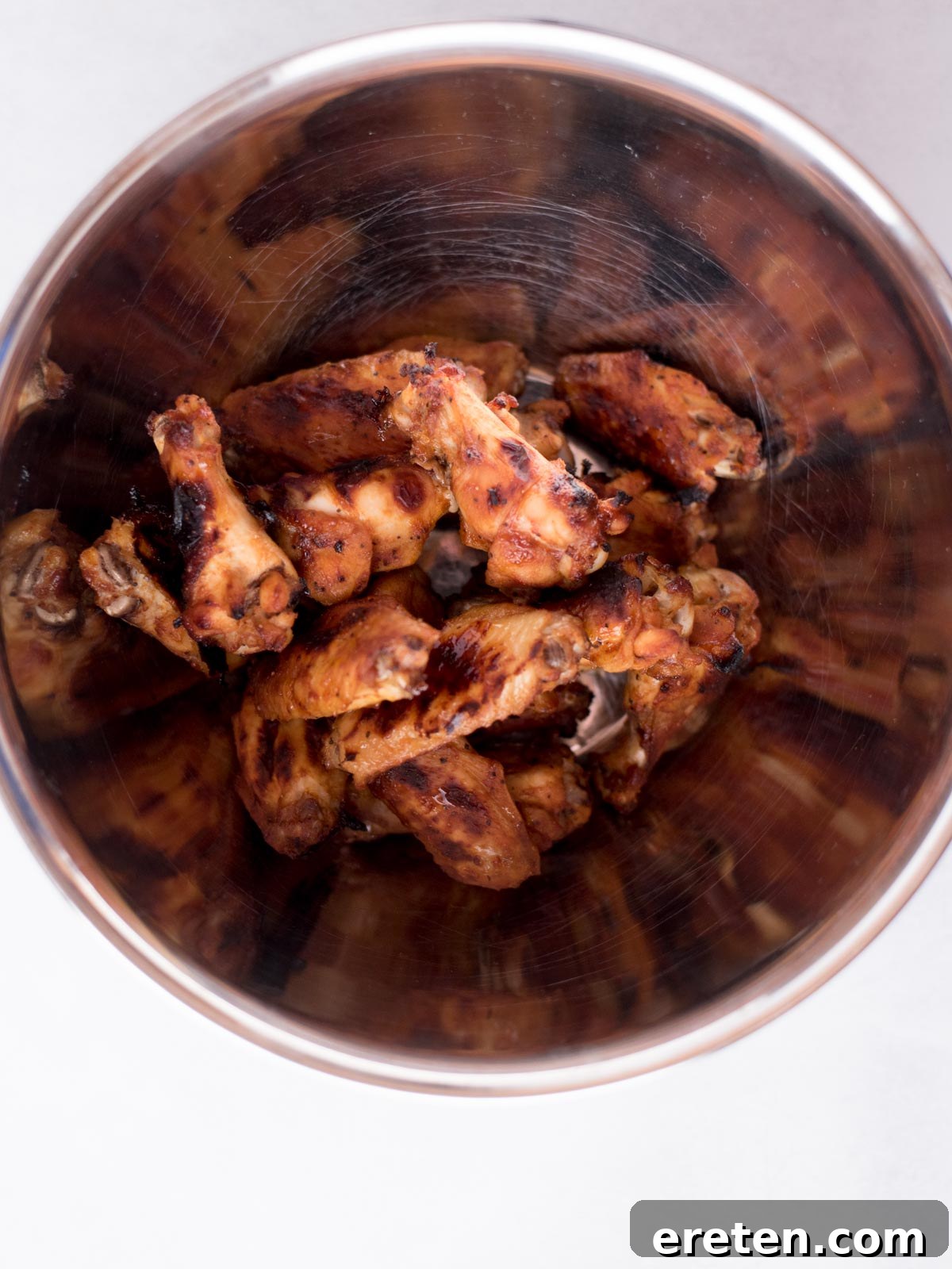 A generous serving of cooked BBQ chicken wings, with glistening caramelized sauce, gathered together in a large mixing bowl, ready for a final toss or serving.