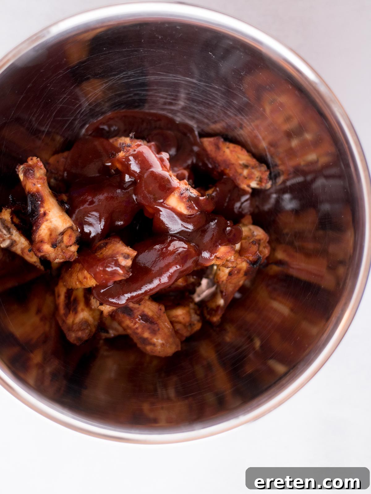 Cooked BBQ chicken wings in a mixing bowl, generously topped with an additional pour of rich barbecue sauce, ready for a final toss to achieve maximum glaze and flavor.