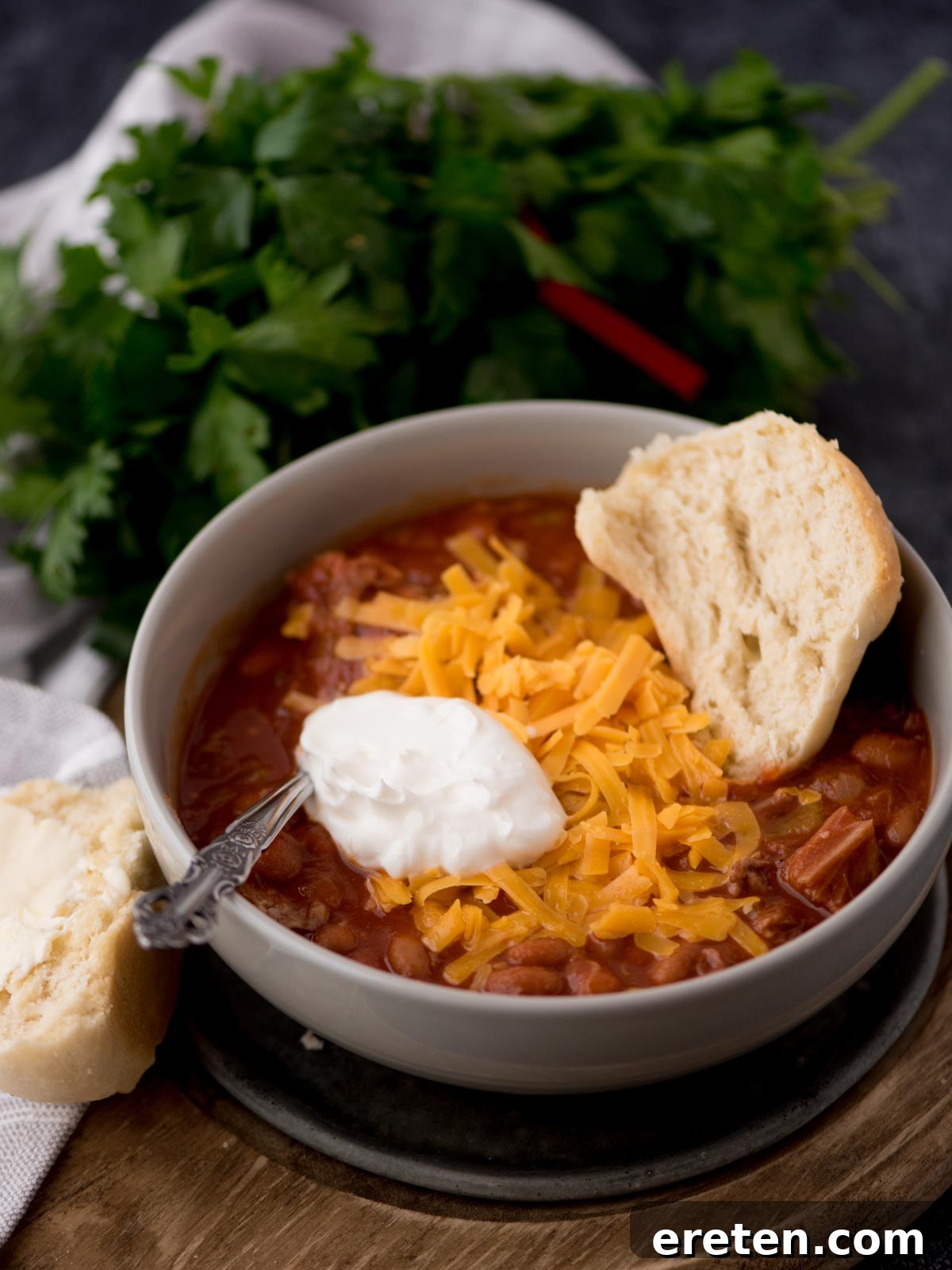 brisket chili in a grey bowl topped with sour cream, shredded cheese, and half of a buttered roll