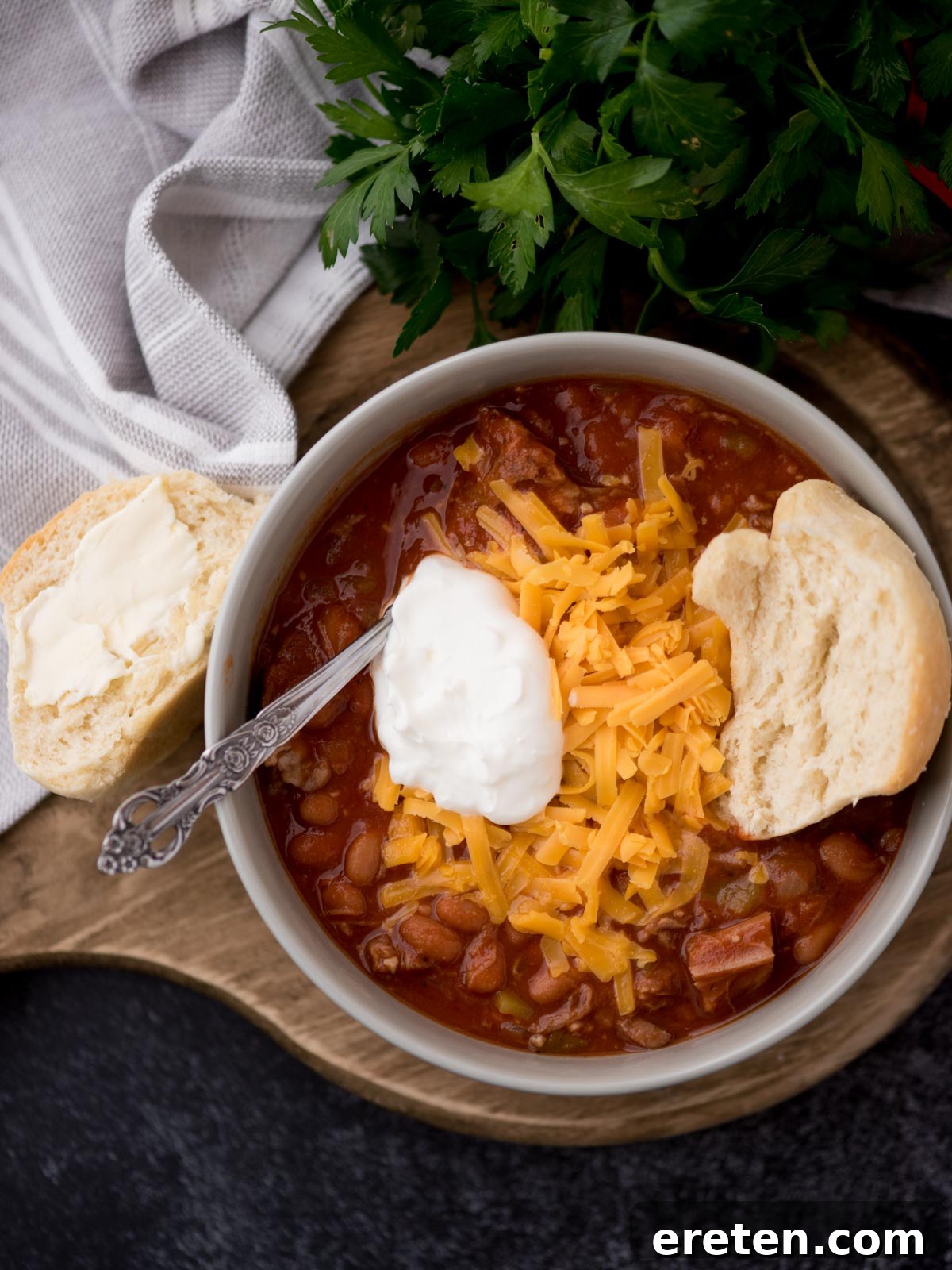 brisket chili in a grey bowl topped with shredded cheddar, sour cream, and half of a buttered roll