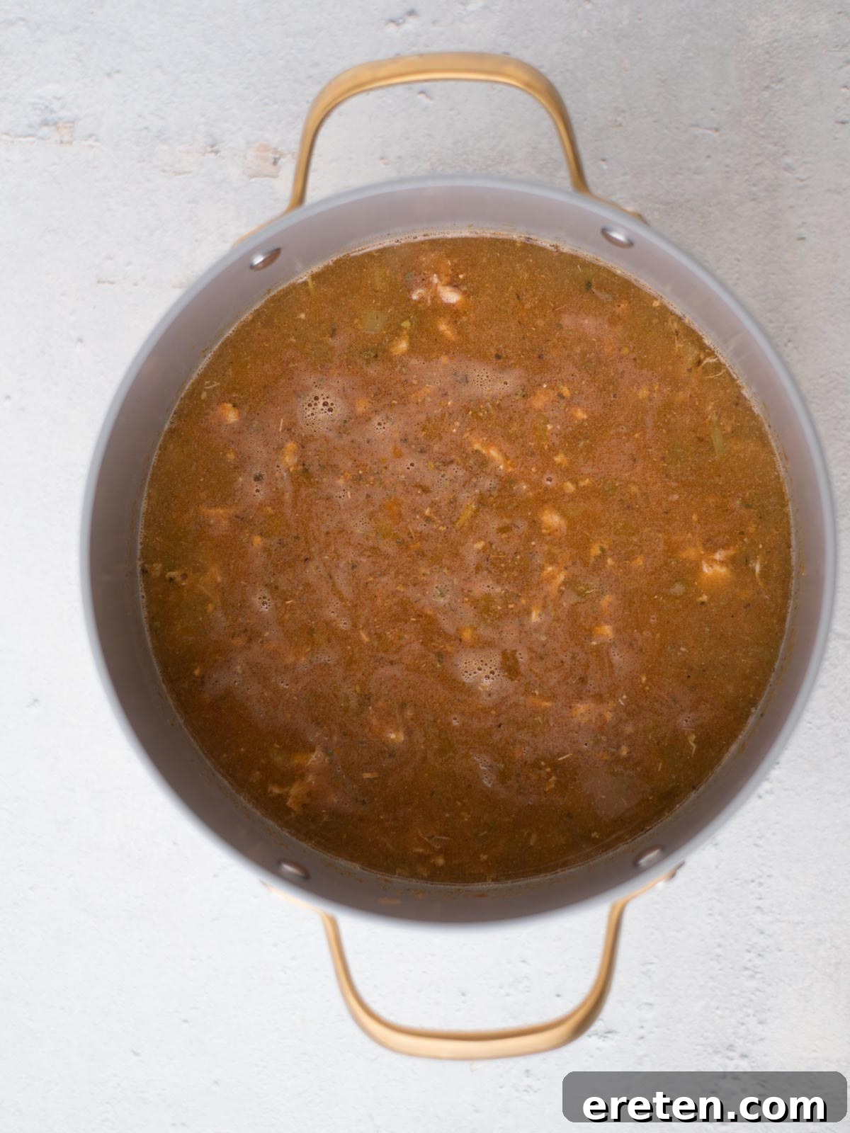 A large, rustic pot filled with simmering, savory white chicken chili, showcasing tender pieces of chicken and vibrant vegetables gently bubbling in a rich, creamy broth. The pot, equipped with two sturdy handles for easy lifting, is gracefully positioned on a smooth, light grey surface, exuding warmth and culinary delight.