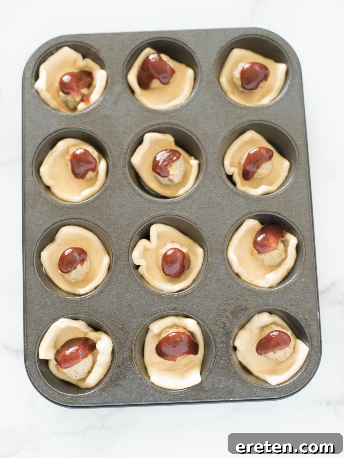 Touchdown BBQ Meatball Crescents 6 BBQ sauce drizzled over meatballs in crescent dough in a muffin tin, ready to bake.