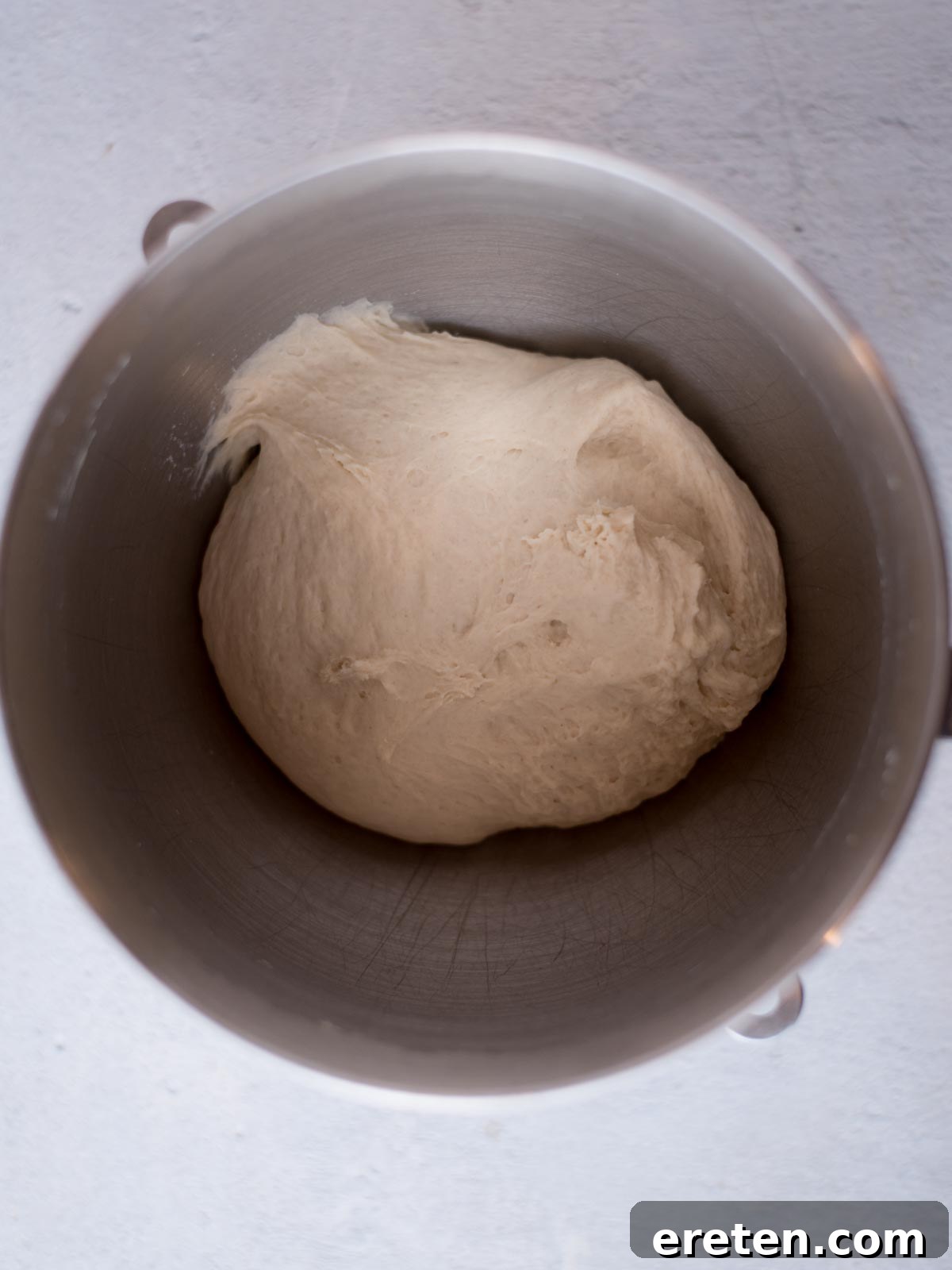 Smooth and elastic dough in a mixing bowl after being kneaded, indicating proper gluten development for soft yeast rolls.