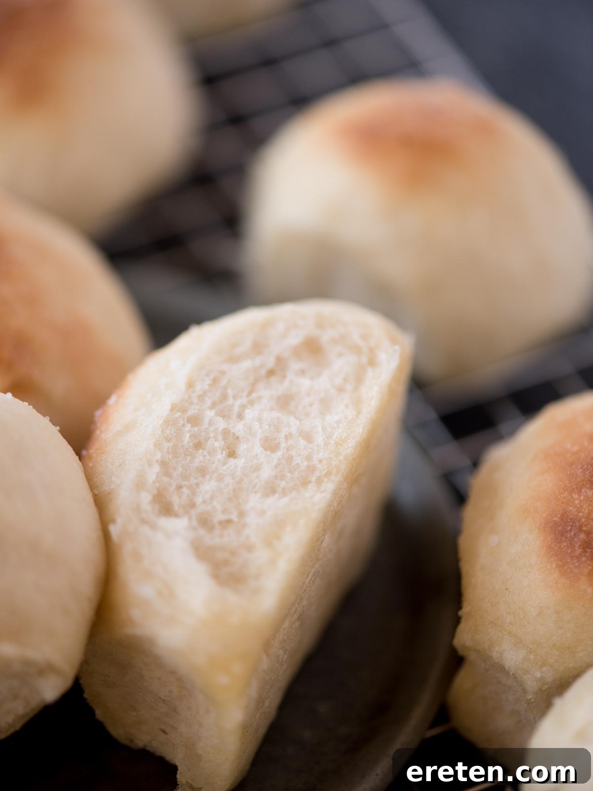 A single, perfectly baked, light and fluffy homemade yeast roll resting on its side on a clean white plate, ready to be eaten.