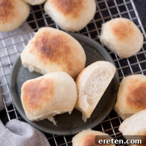 Homemade yeast rolls on a plate, resting on a cooling rack next to a kitchen towel