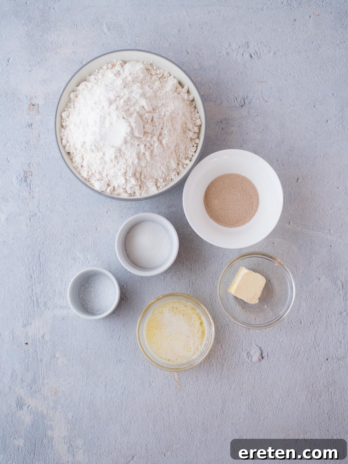 Bowls of essential ingredients including warm water, yeast, sugar, butter, salt, and all-purpose flour, neatly arranged for homemade yeast rolls.