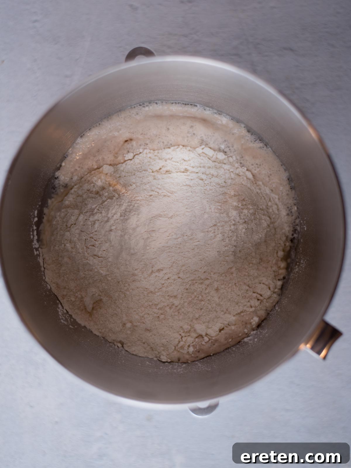 All-purpose flour being added to the activated yeast mixture in a large mixing bowl, preparing for dough formation.