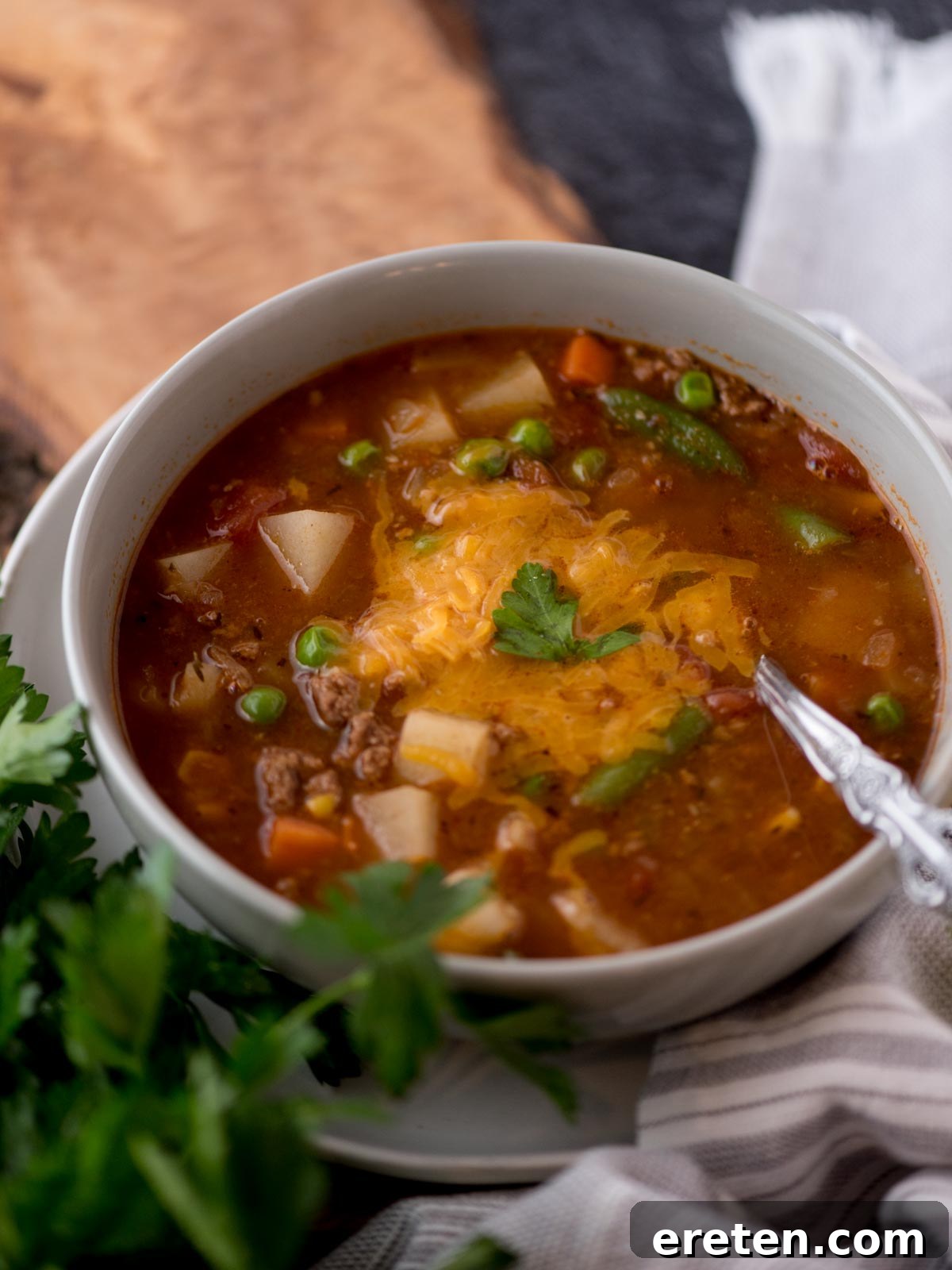 Hearty Hamburger Vegetable Soup 2 Hearty hamburger soup in a rustic grey bowl, garnished with freshly shredded cheddar cheese and vibrant green parsley.
