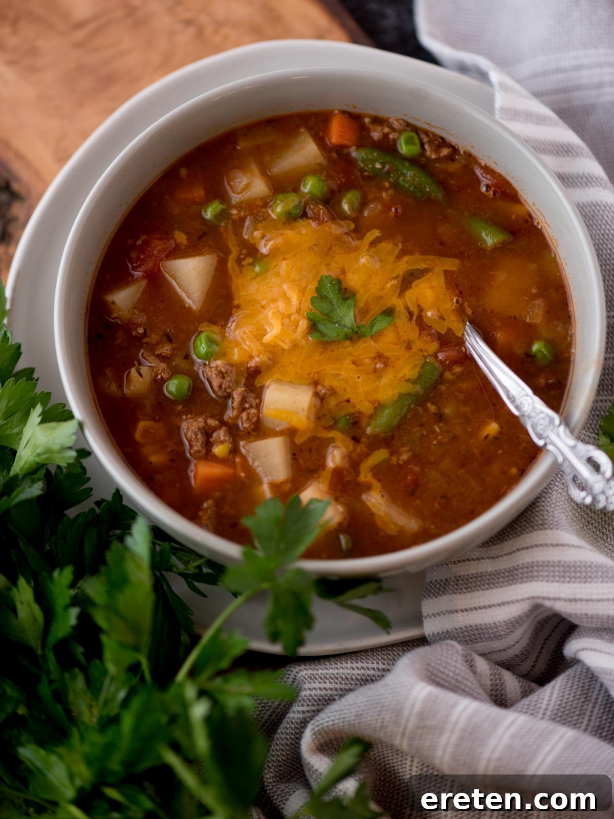 Hearty Hamburger Vegetable Soup 7 A steaming bowl of flavorful hamburger soup, generously topped with melted shredded cheese and fresh green parsley, invitingly presented.