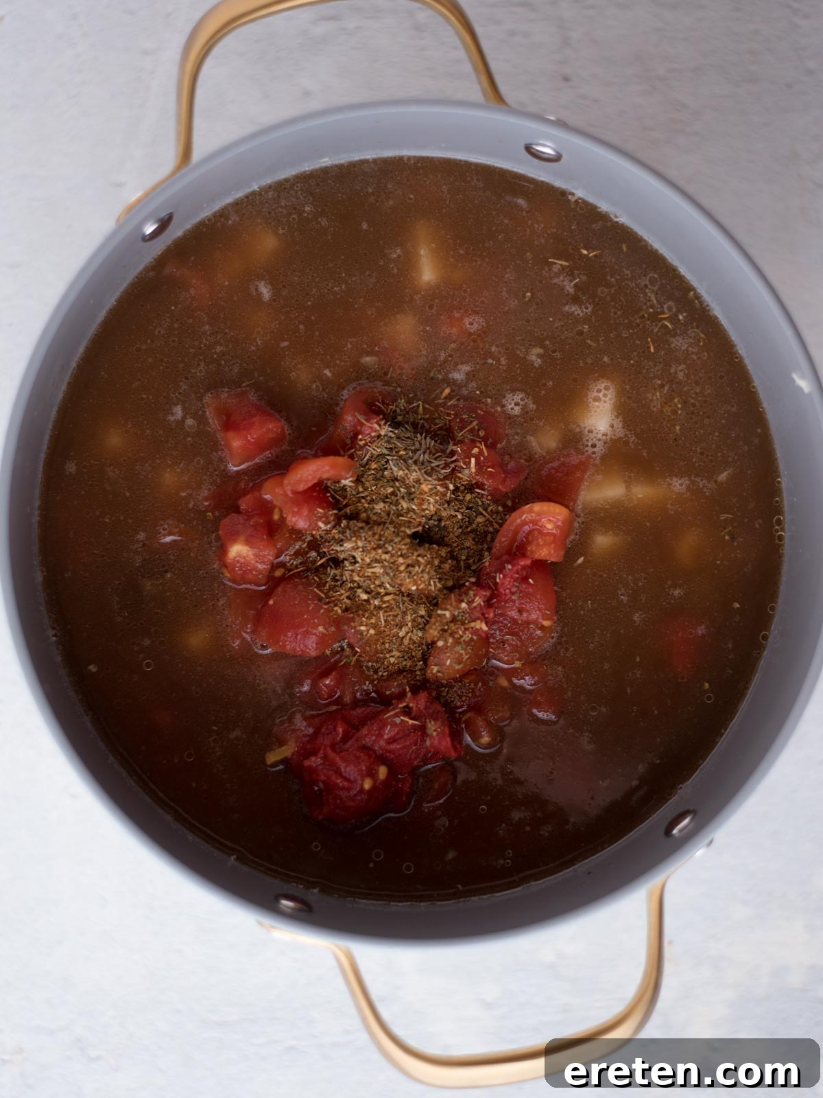 Hearty Hamburger Vegetable Soup 5 A birds-eye view into a large stock pot showing the rich broth, diced potatoes, seasoned ground beef, celery, and onion simmering together.