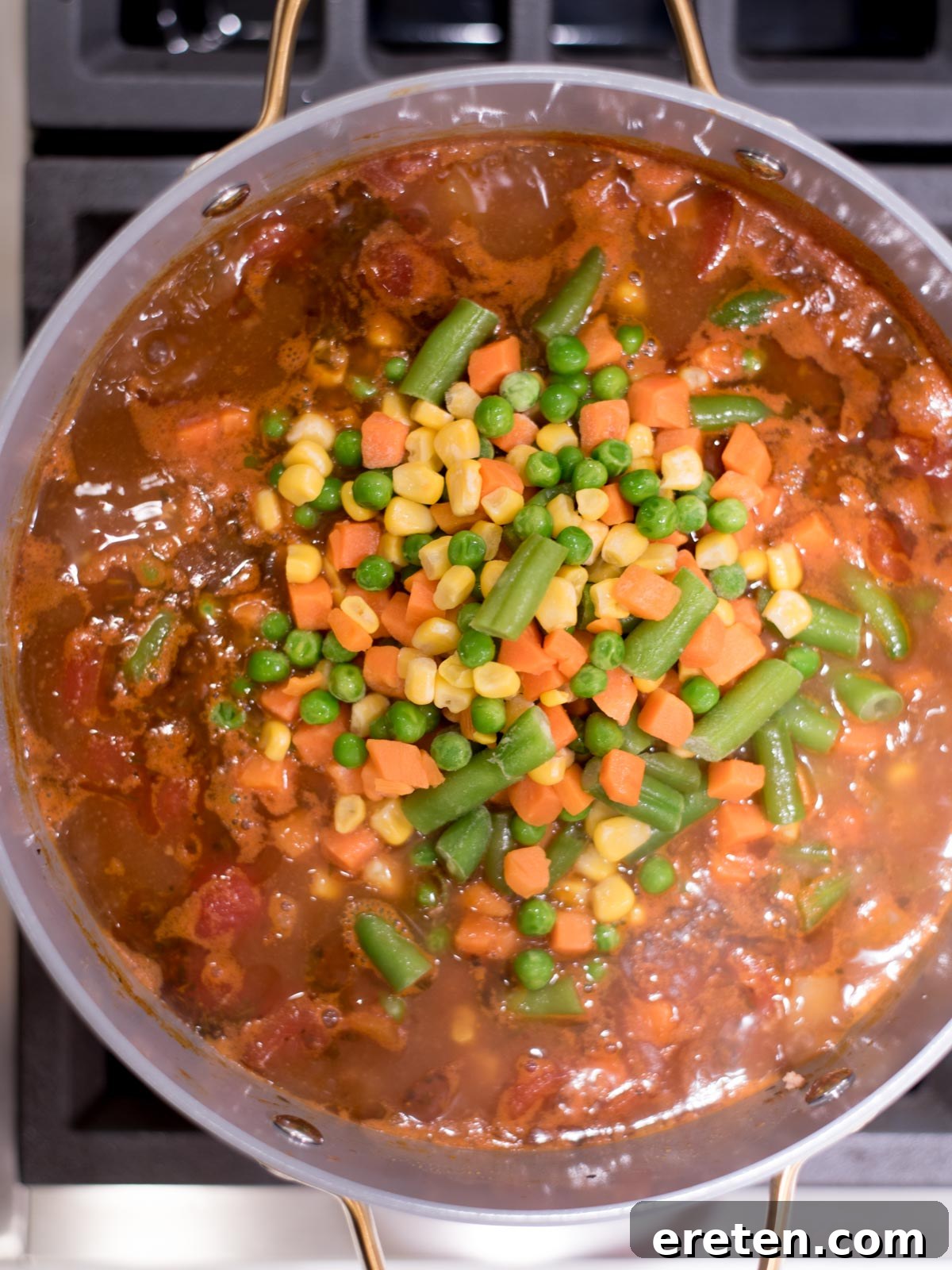 Hearty Hamburger Vegetable Soup 6 Hamburger soup simmering gently in a large pot on the stove, steam rising, with the frozen vegetables yet to be stirred in, showcasing its rich, deep color.