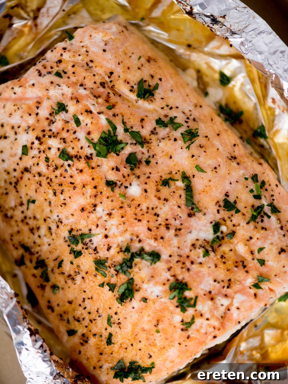 baked salmon in foil on a baking sheet surrounded by fresh parsley and a kitchen towel