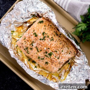 baked salmon in foil on a baking sheet surrounded by fresh parsley and a kitchen towel