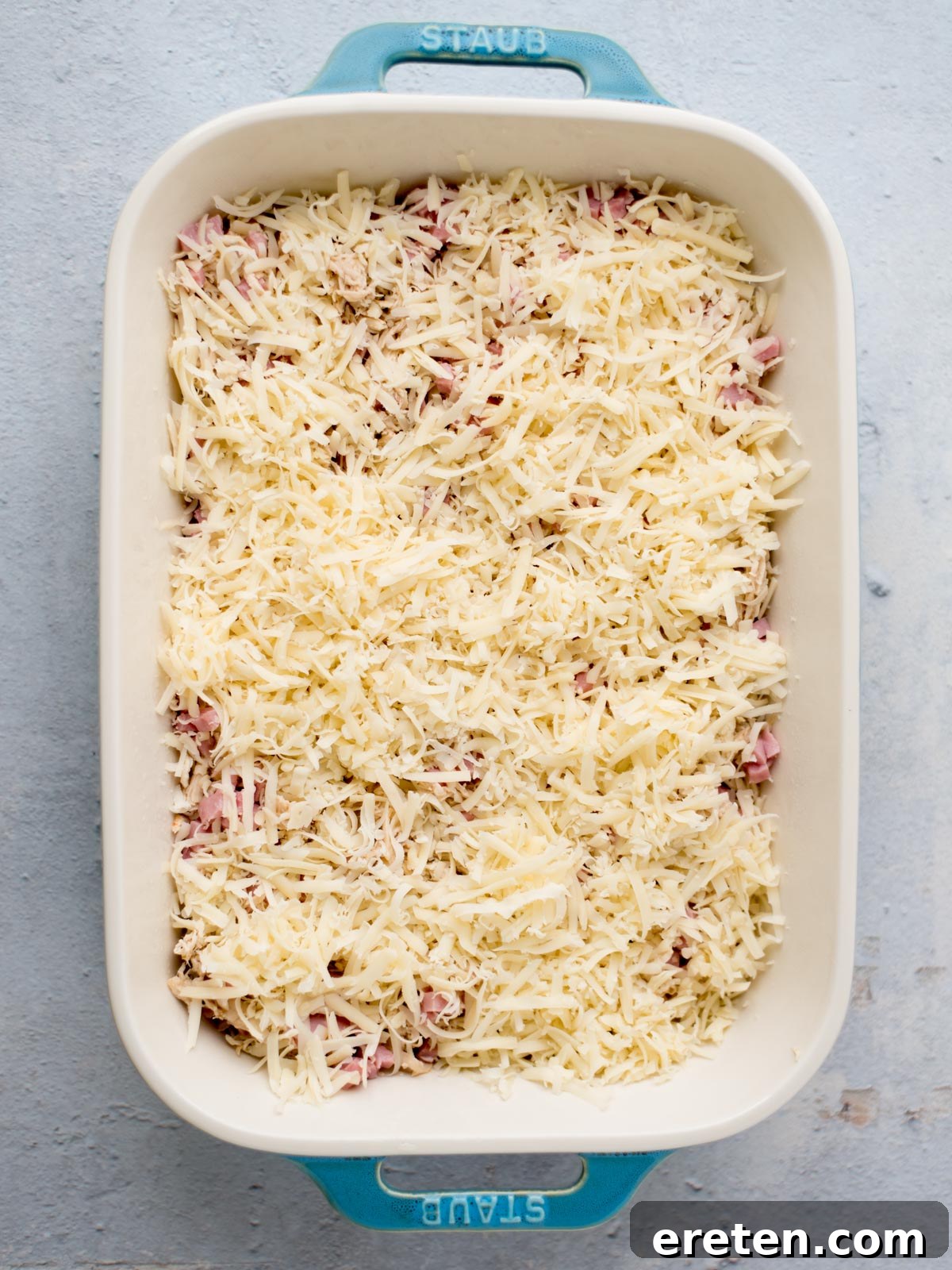 assembly of chicken cordon bleu casserole where the chicken, ham, and Swiss are in the baking dish