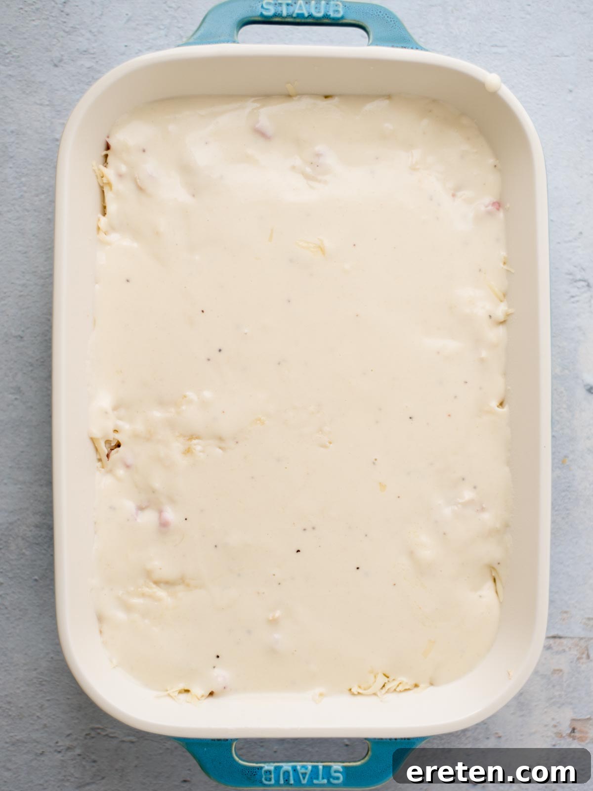 chicken cordon bleu casserole assembly where the sauce has been poured over the Swiss cheese