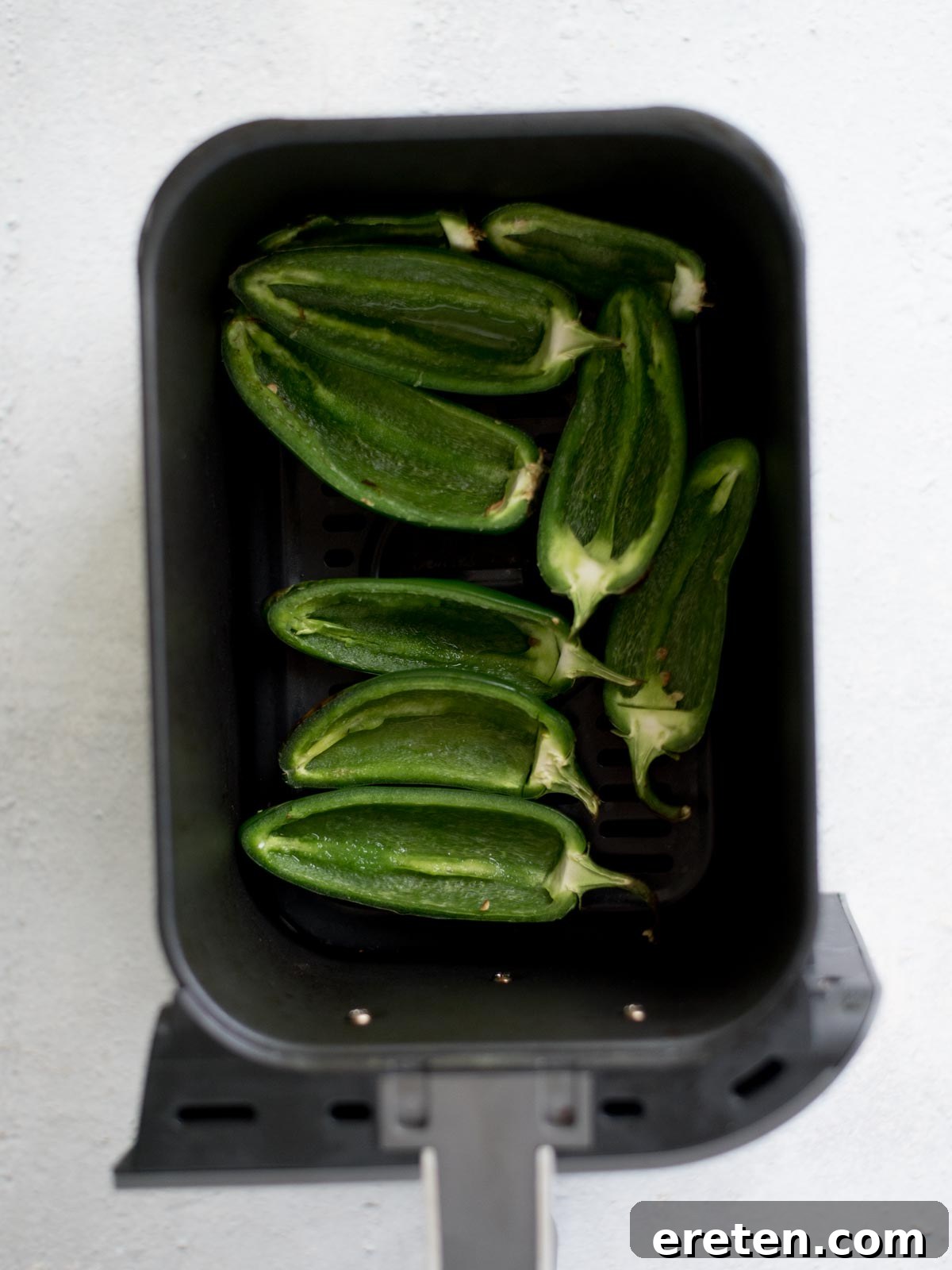 Par-baked jalapenos arranged in an air fryer basket