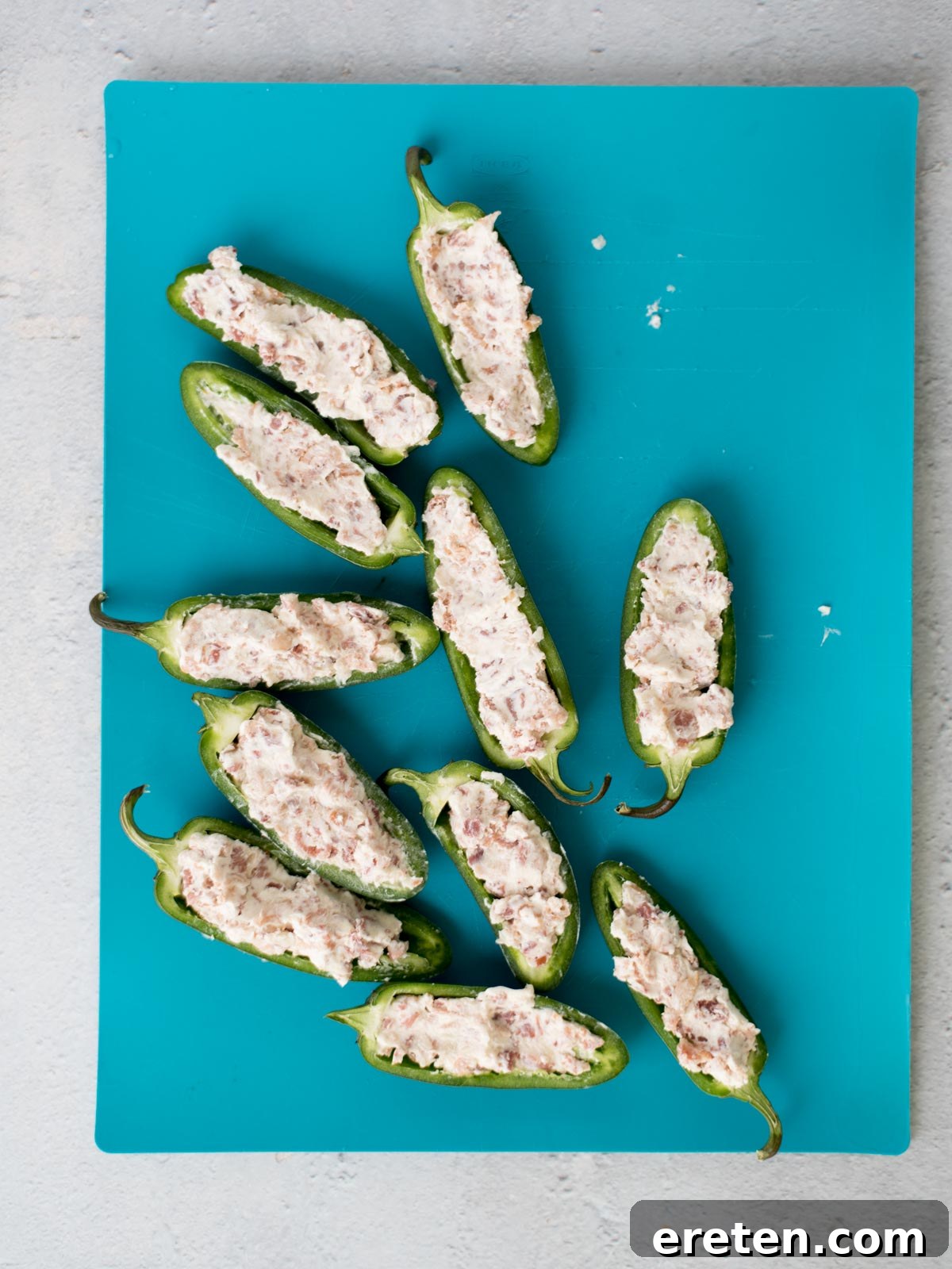 Stuffed jalapeno halves with cheese and bacon on a cutting board