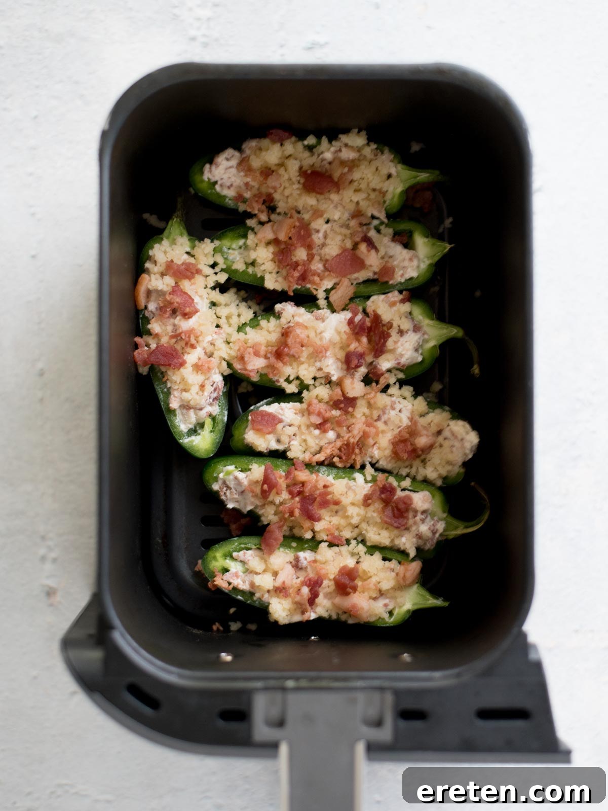 Uncooked jalapeno poppers with breadcrumb topping in an air fryer basket