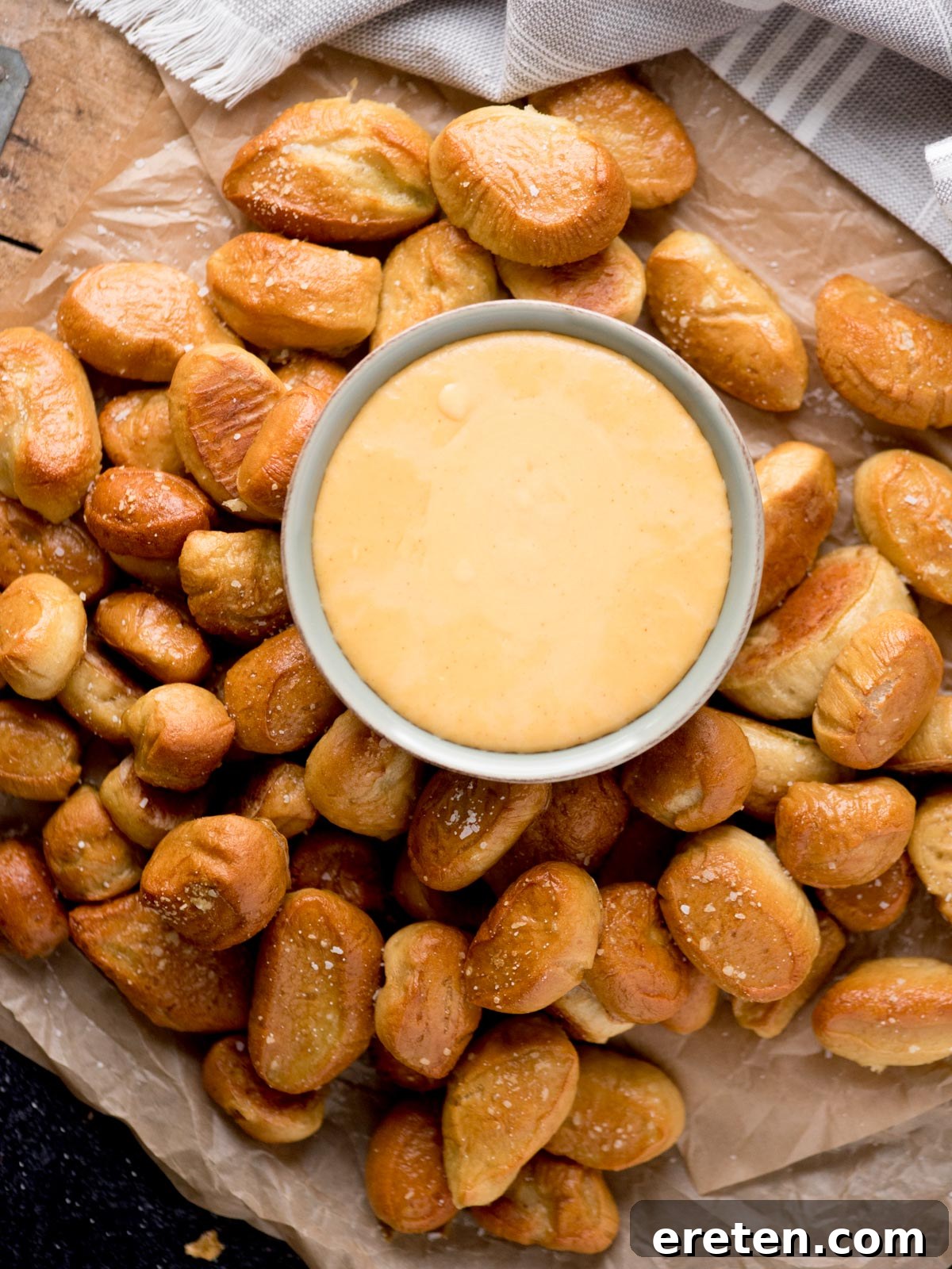 A golden beer cheese dip in a rustic bowl, surrounded by fluffy soft pretzel bites on parchment paper, ready for dipping.