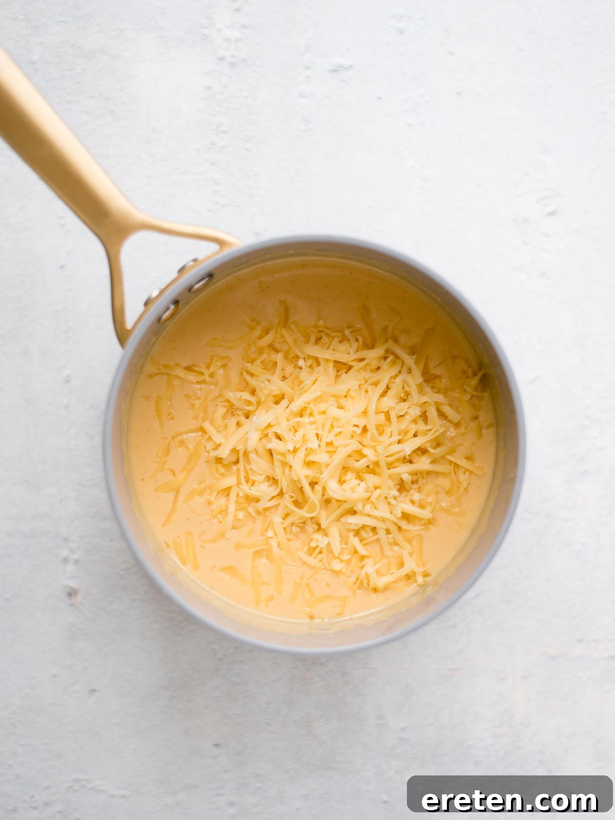 Shredded smoked gouda cheese melting into the rich beer cheese dip in the saucepan, completing the cheesy blend.