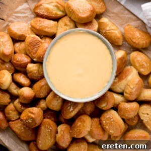 Beer cheese dip in a bowl surrounded by soft pretzel bites on parchment paper