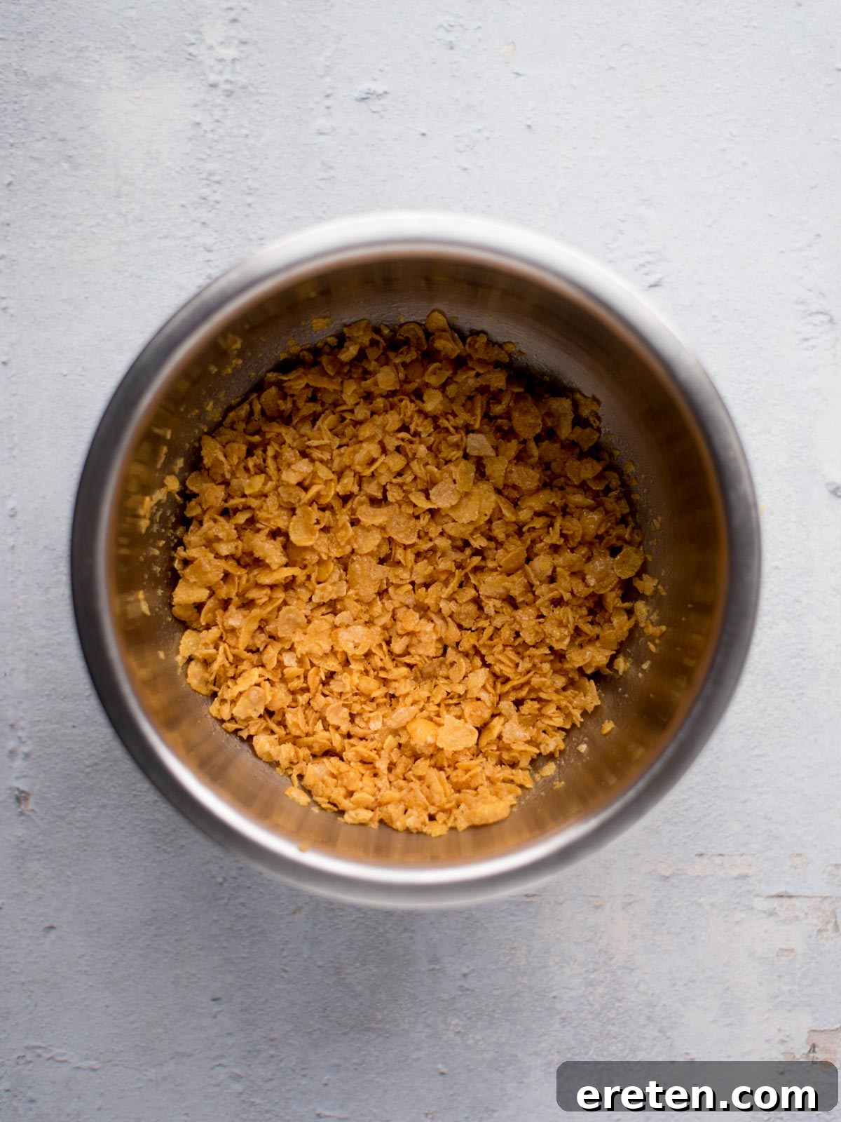 Crushed cornflakes and melted butter mixed together in a small mixing bowl, ready to become the crispy topping.