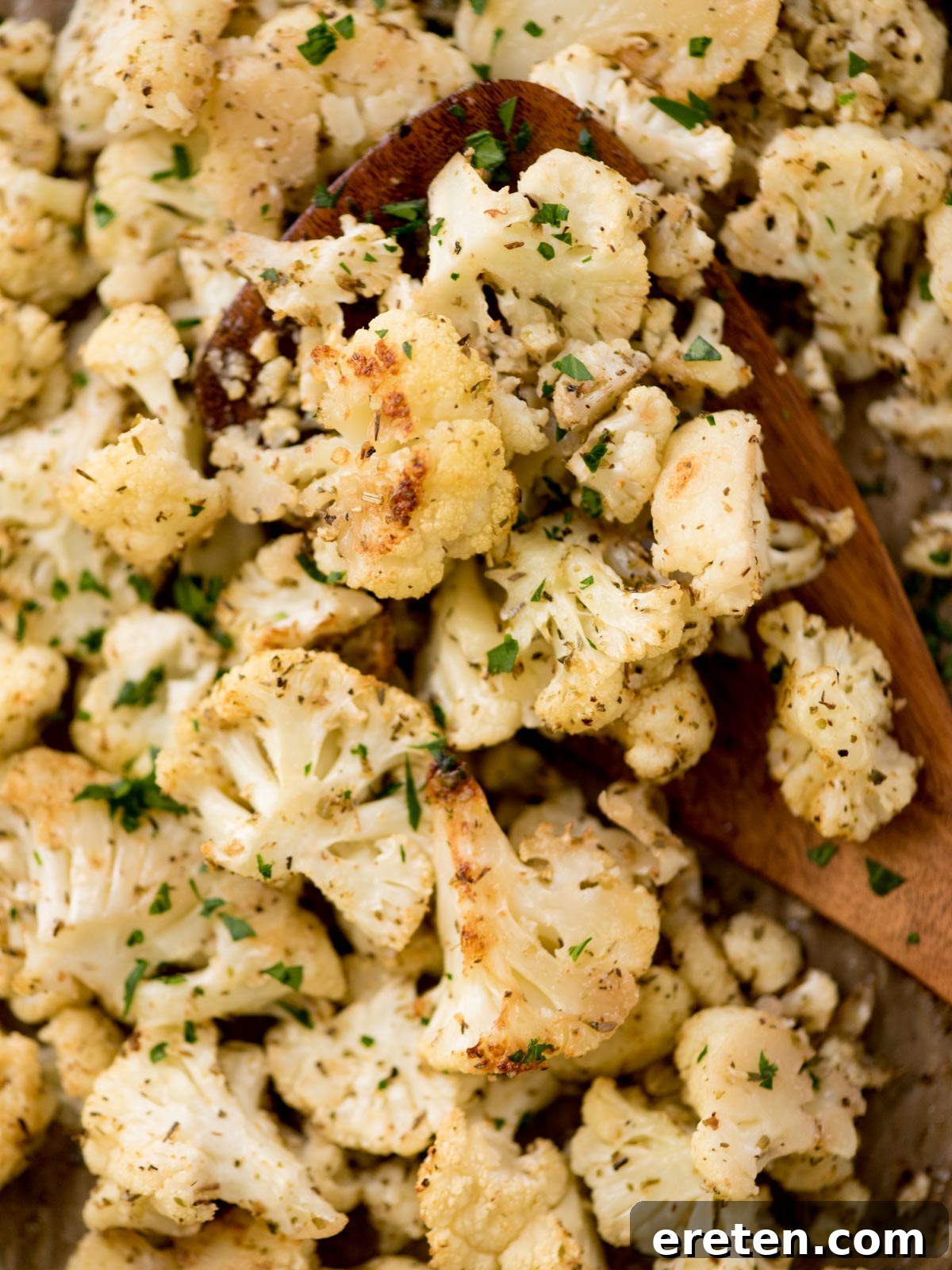 roasted cauliflower being scooped from a baking sheet, golden brown and crispy