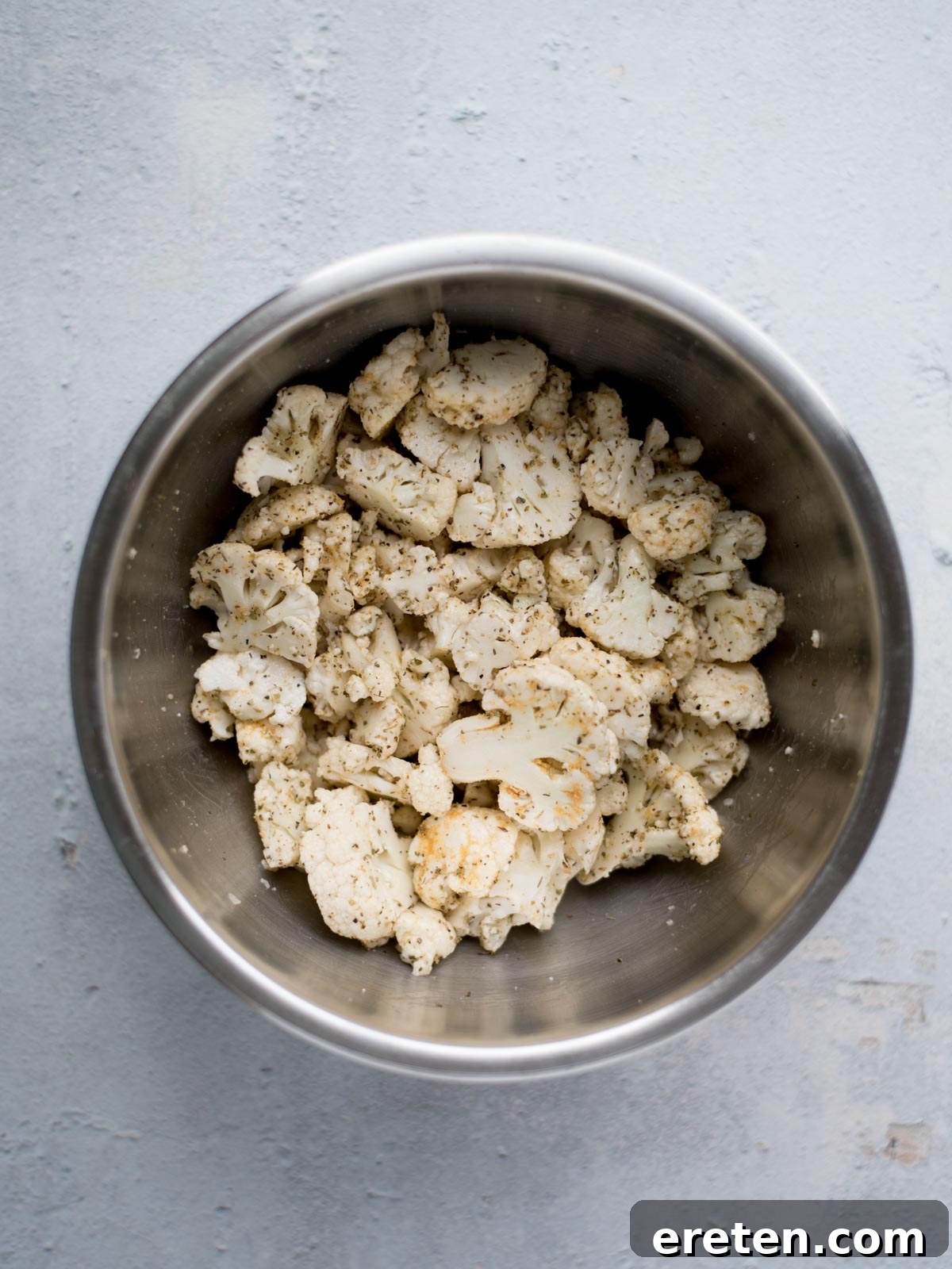 seasoned chopped cauliflower in a mixing bowl with more spices