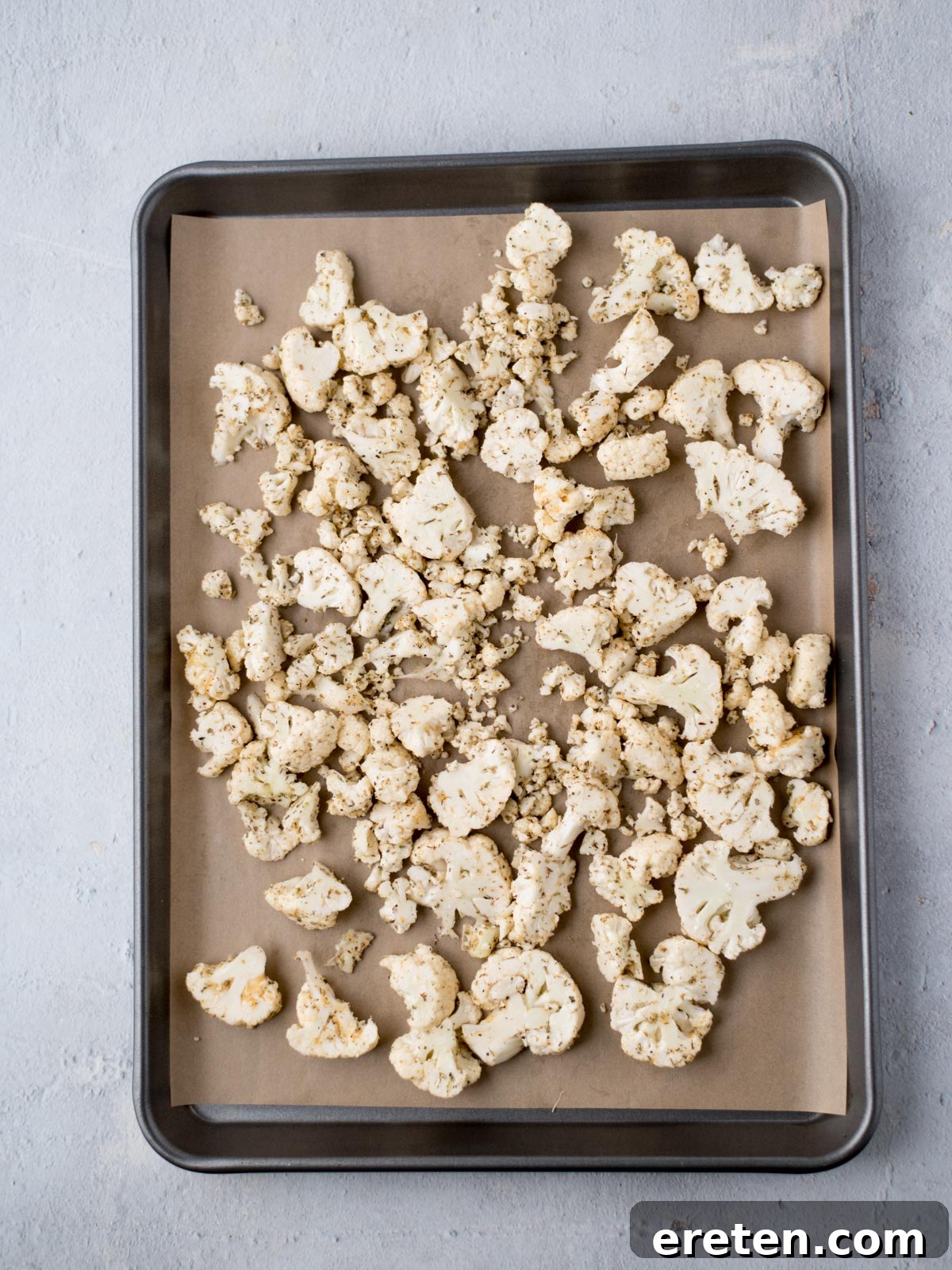 uncooked, seasoned cauliflower on a parchment lined baking sheet, spread in a single layer