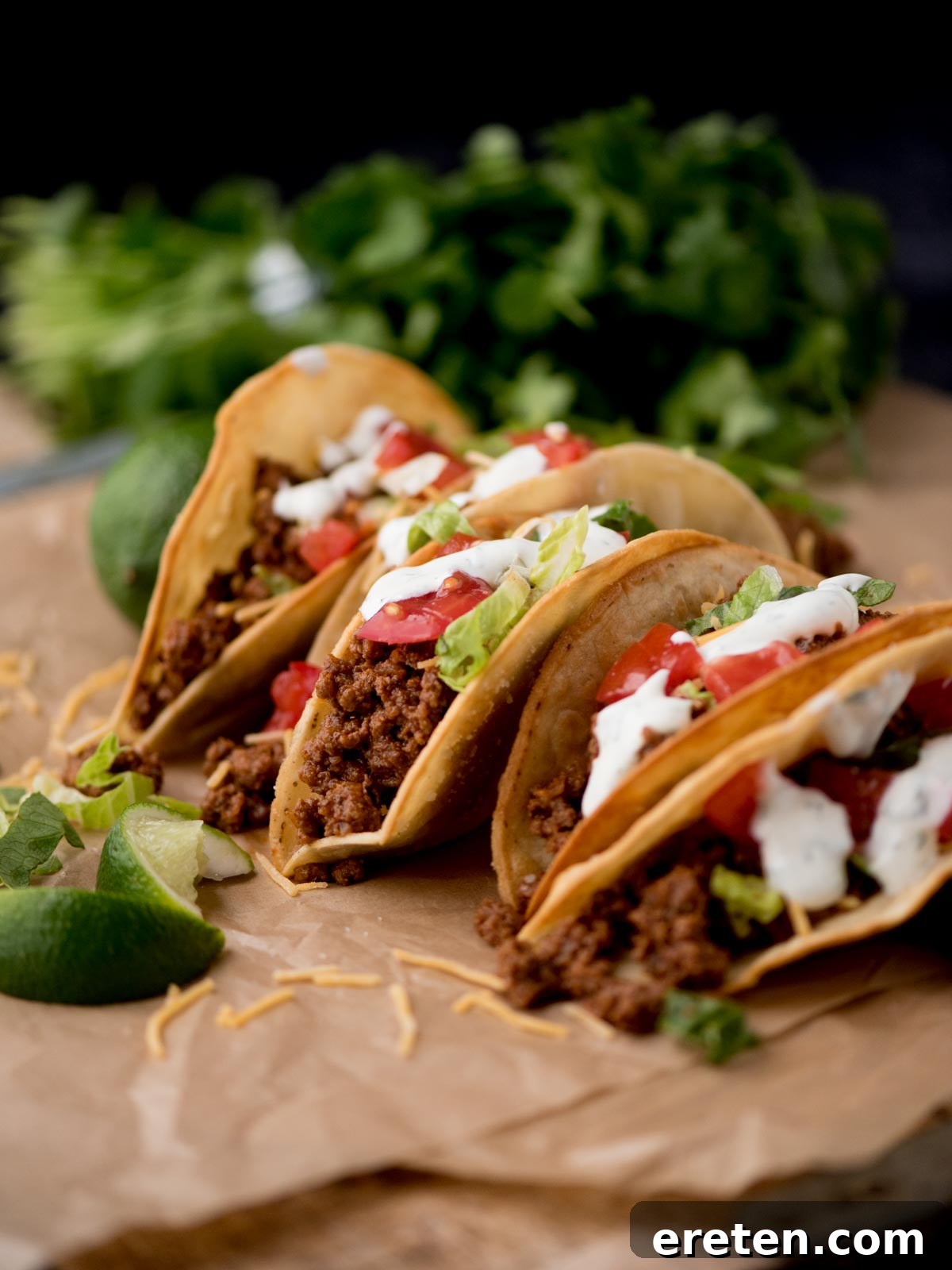 Flavorful ground beef tacos arranged on parchment paper, garnished with fresh cilantro and lime wedges, ready to be served.