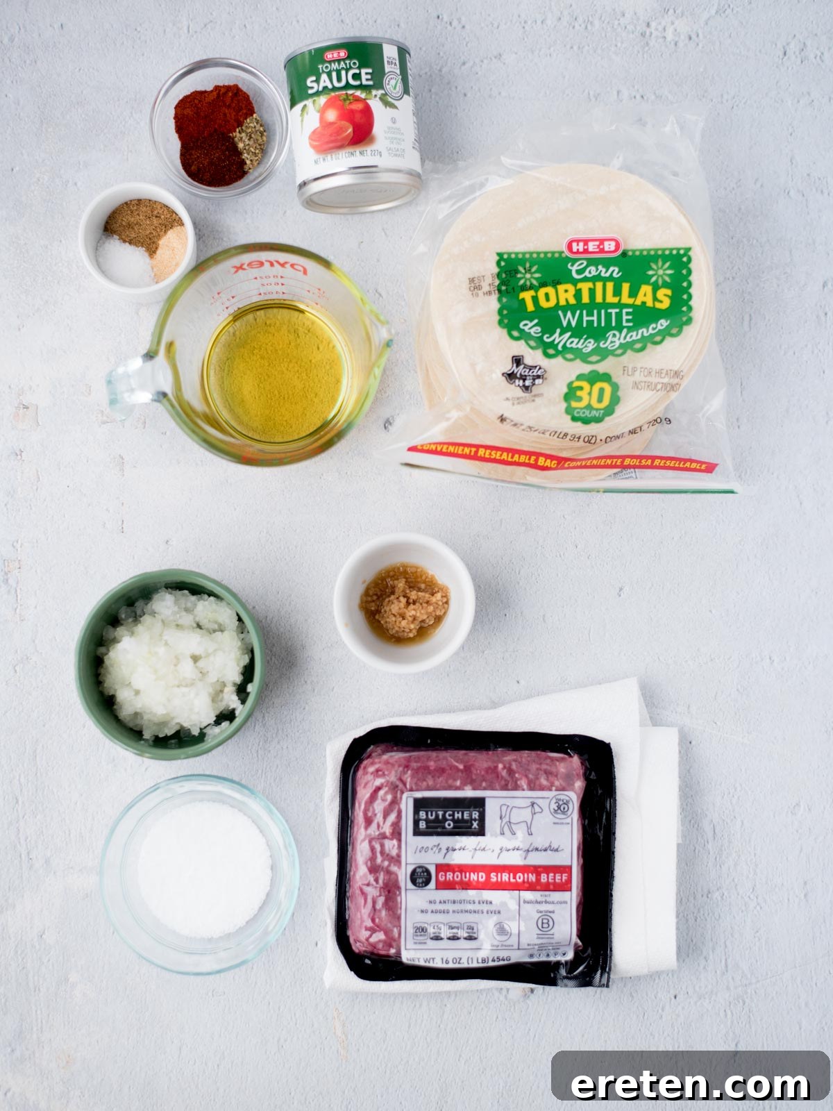 Arrangement of fresh ingredients for ground beef tacos, including ground beef, diced onion, garlic, and various spices.
