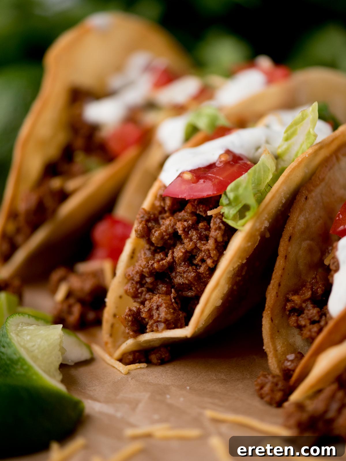 Ground beef tacos artfully arranged on parchment paper, surrounded by fresh cilantro and lime wedges for garnish.