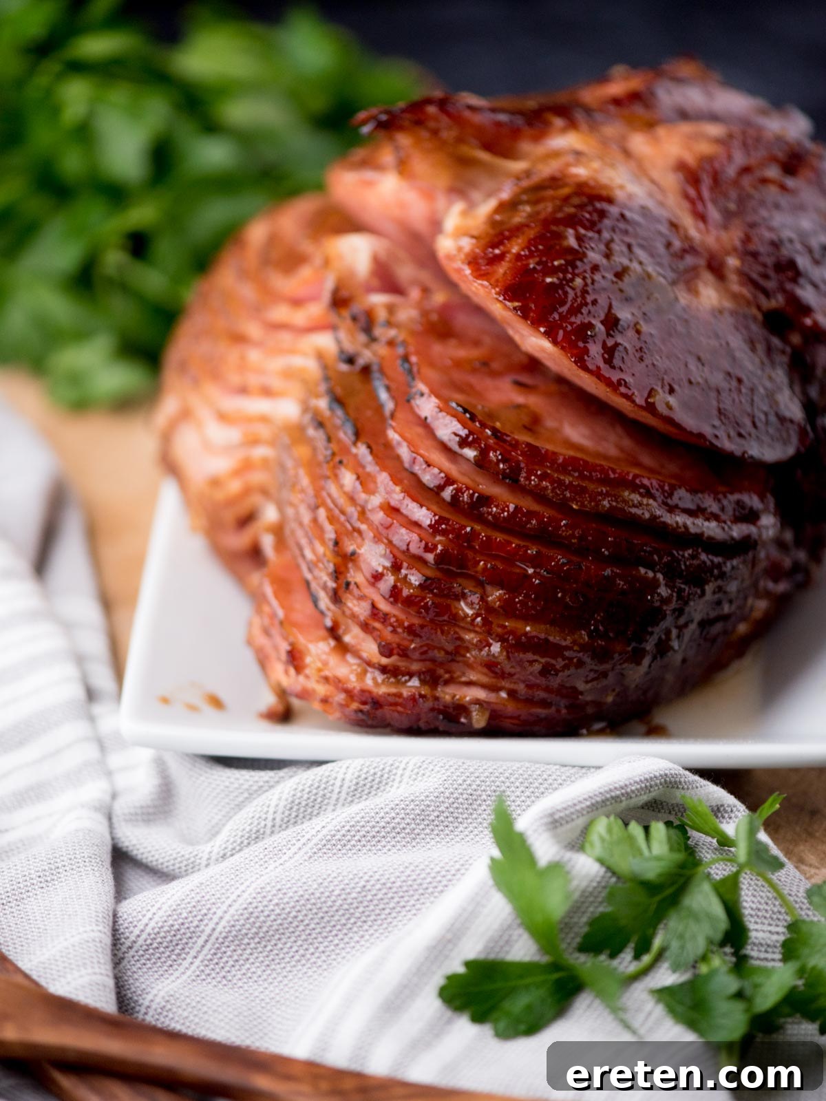 Beautifully glazed brown sugar ham on a plate, garnished with fresh parsley and a kitchen towel