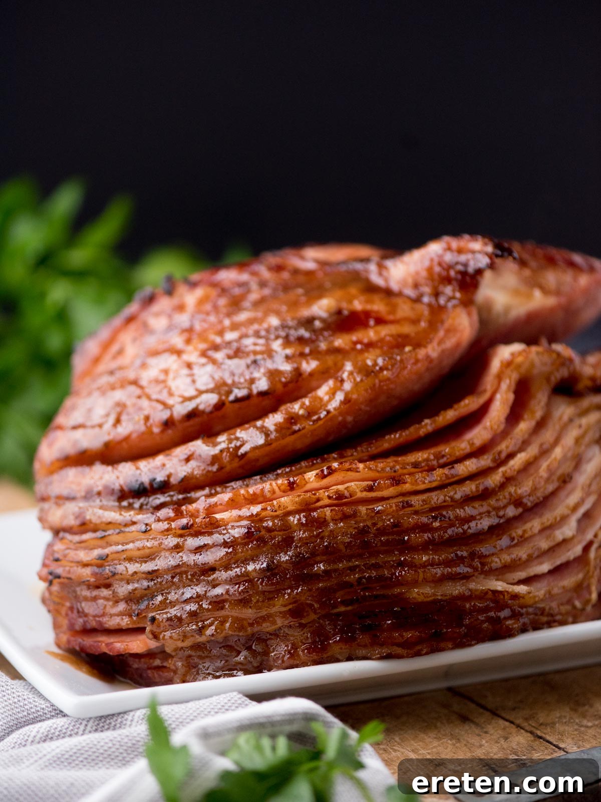 Serving of brown sugar glazed ham on a plate with parsley and kitchen towel