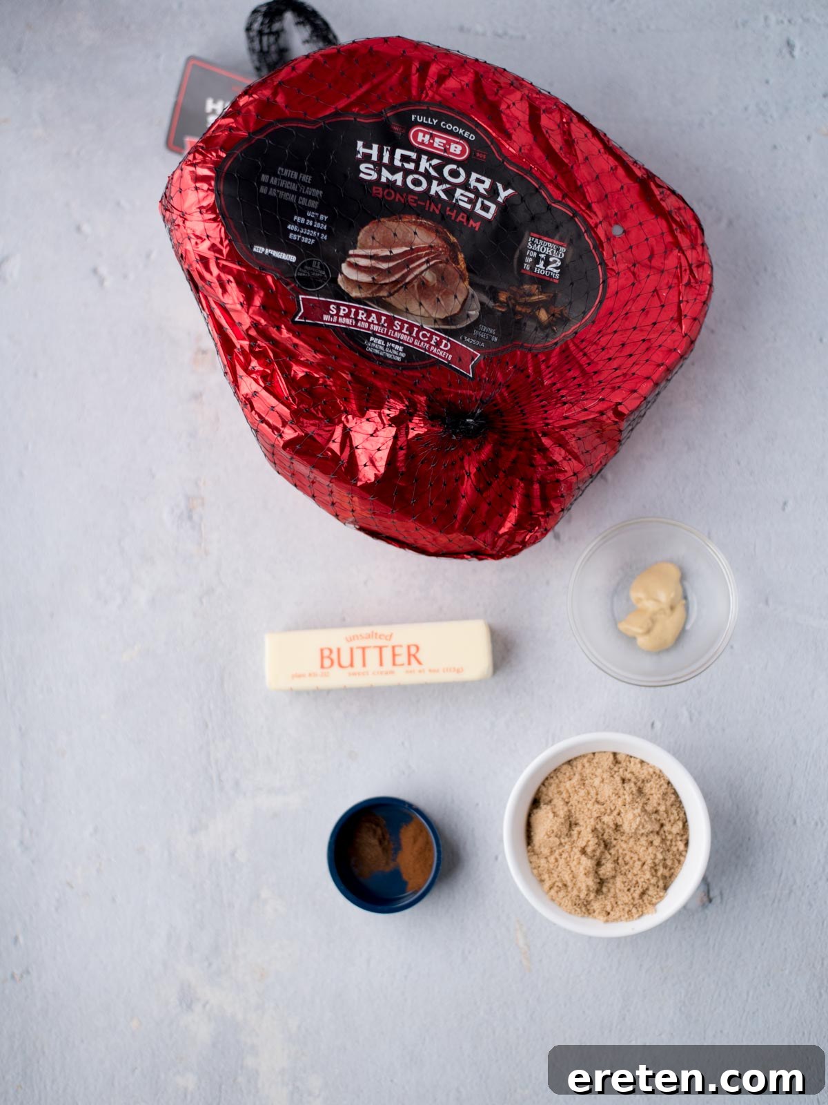 Ingredients laid out for making brown sugar glazed ham: brown sugar, butter, cinnamon, allspice, dijon mustard, and a slice of ham.