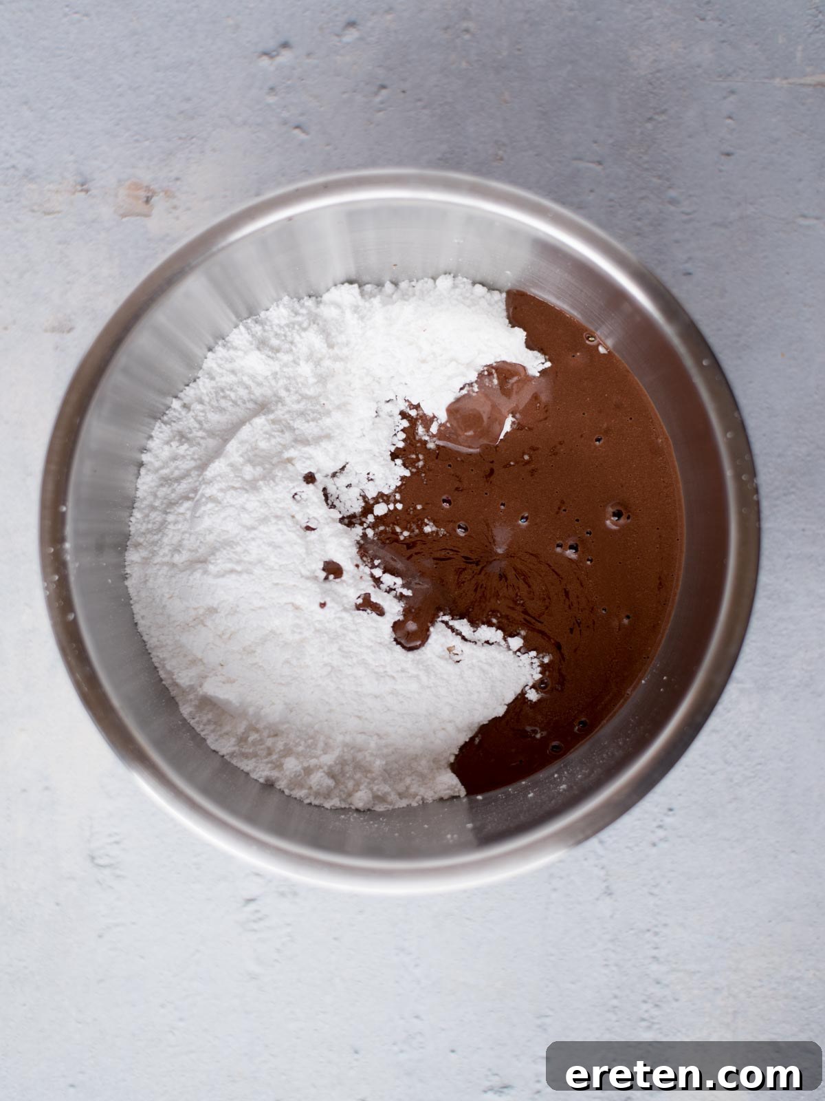 Powdered sugar being mixed with the warm chocolate and buttermilk base in a mixing bowl, creating a smooth, rich Texas Sheet Cake frosting.