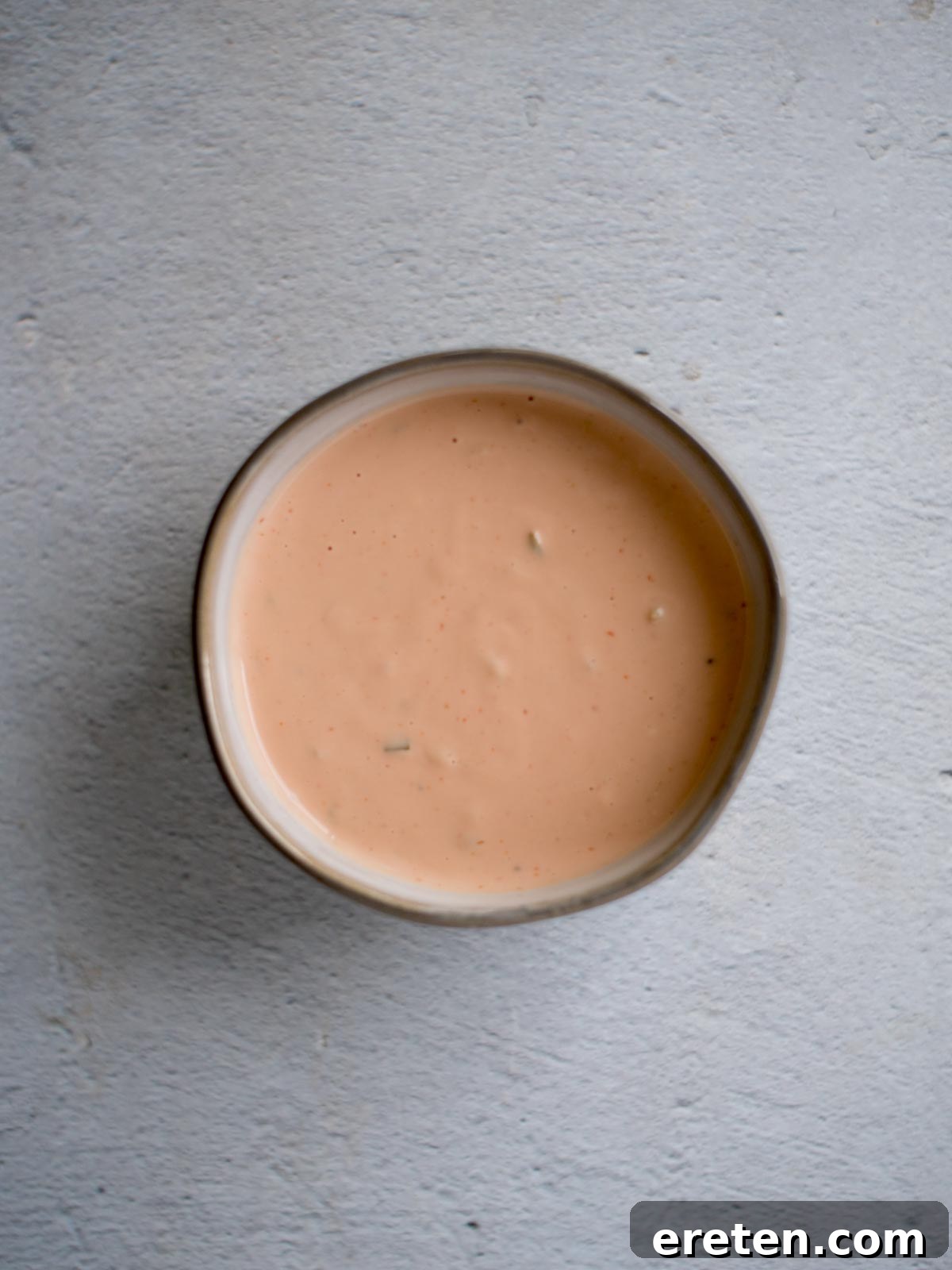 Creamy homemade burger sauce in a ceramic bowl, ready to be served, with a whisk resting next to it.