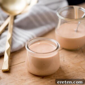 Burger sauce in two glass jars on a bread board, surrounded by a kitchen towel and serving utensils.