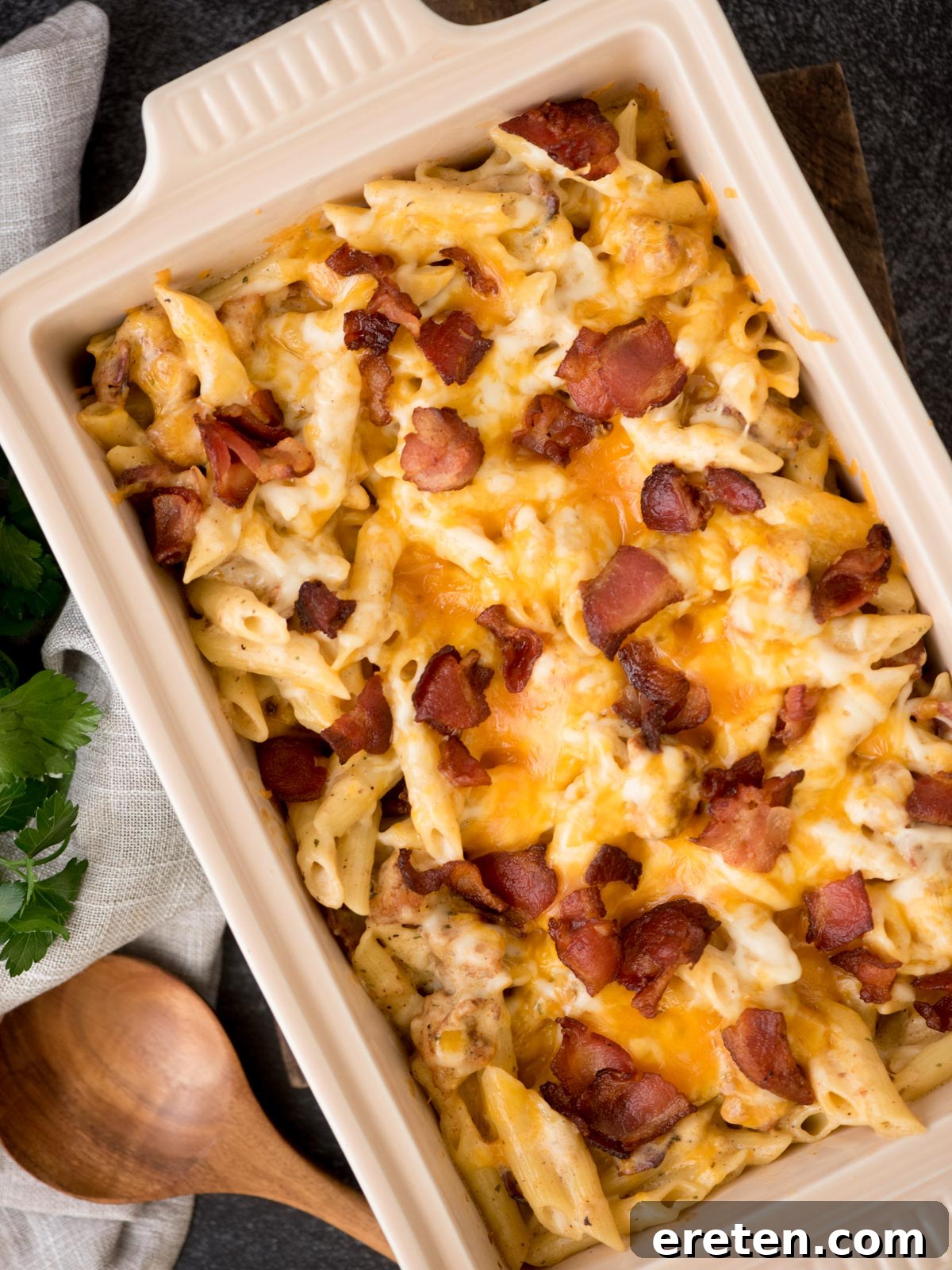 Chicken bacon ranch pasta with melted cheese and bacon over top ready to serve with a wooden spoon resting next to it.