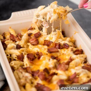 Hand scooping up a serving of chicken bacon ranch pasta with melty cheese pulling away from the baking dish.