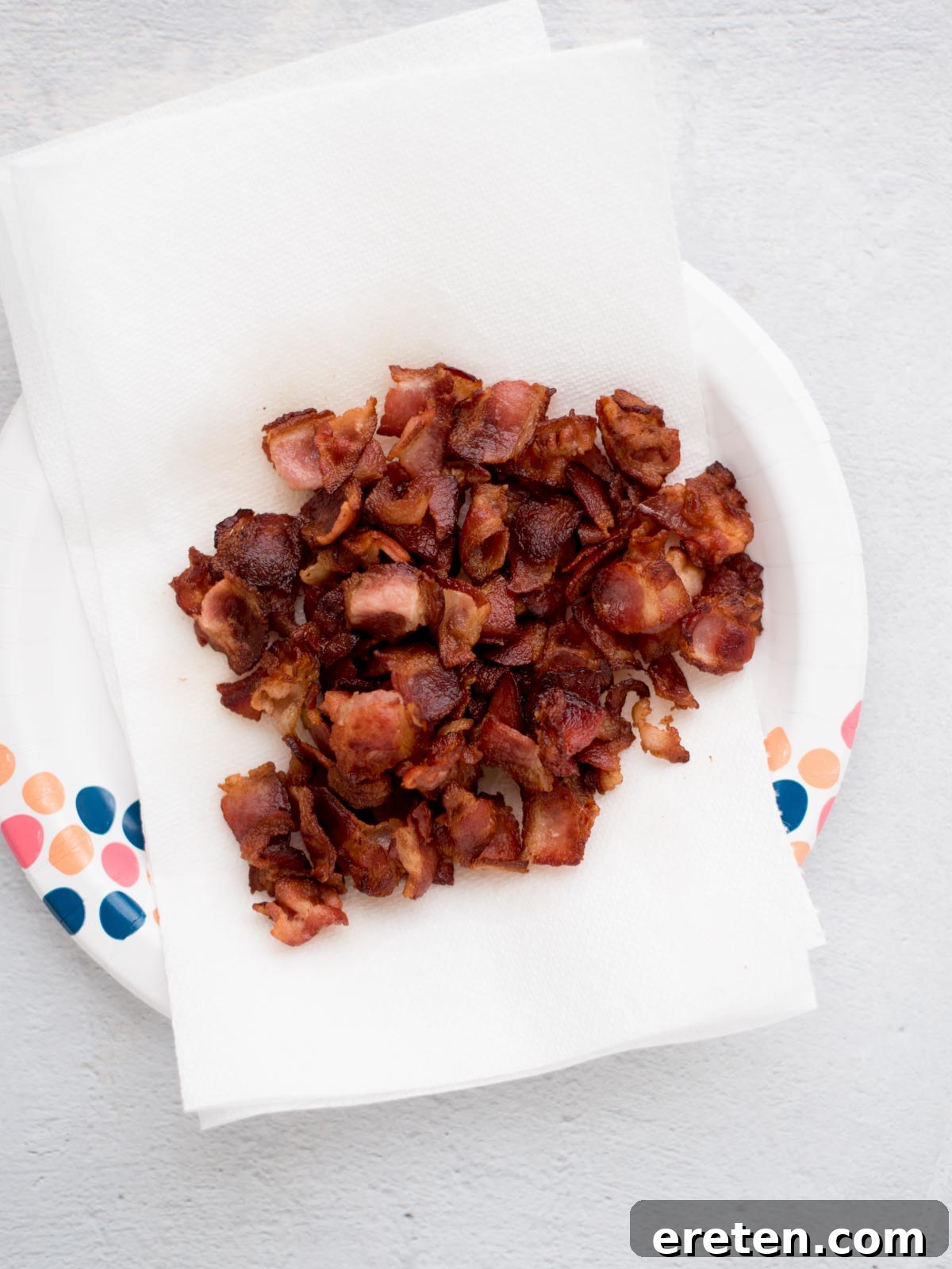 Crispy golden bacon pieces chopped laying on a paper towels covered plate.