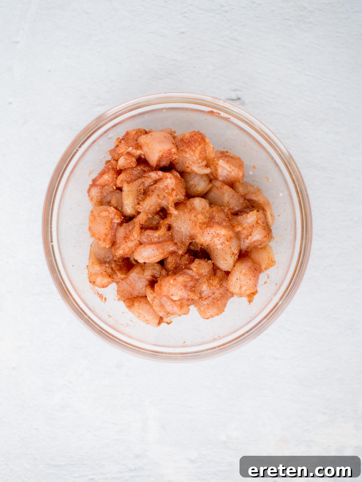 Seasoned raw diced chicken pieces in a mixing bowl.
