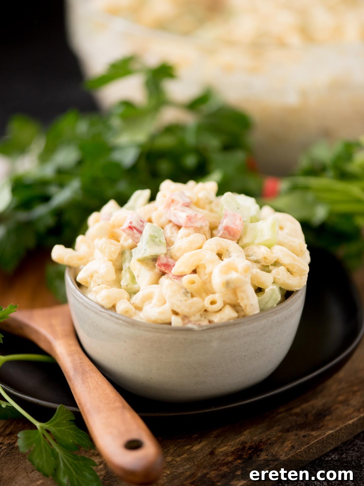 Grandma's Heirloom Macaroni Salad 2 Macaroni salad in a grey bowl surrounded by a serving spoon and fresh parsley.