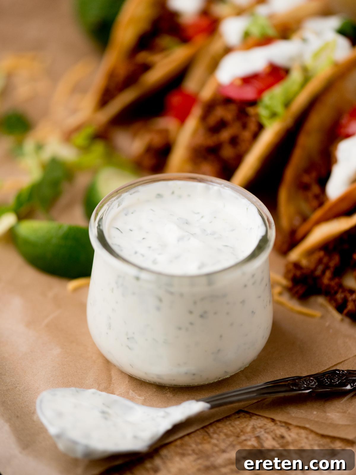 A small glass jar filled with luscious cilantro lime sauce, accompanied by a spoon covered in more of the creamy green sauce resting beside it, ready to be drizzled.