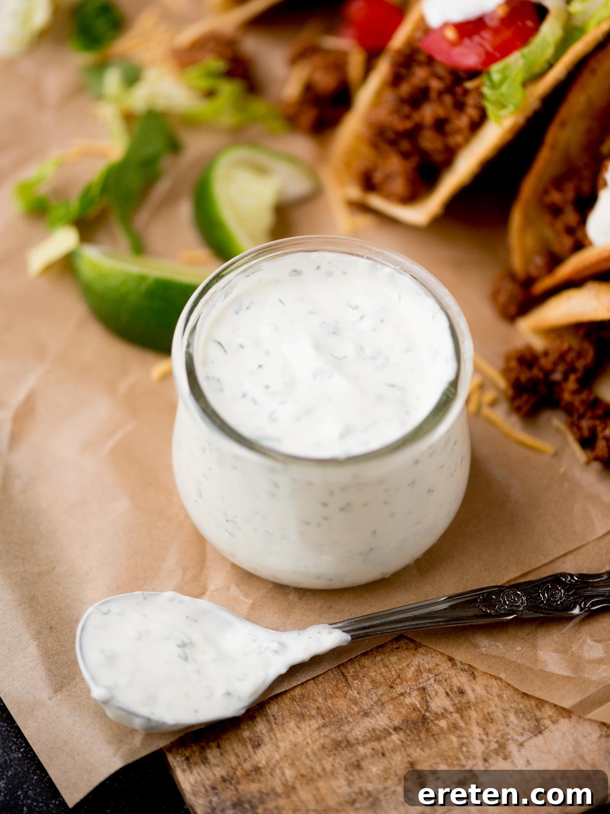 A small glass jar neatly filled with creamy cilantro lime sauce, alongside a spoon covered in the vibrant green sauce, suggesting it's ready for serving.