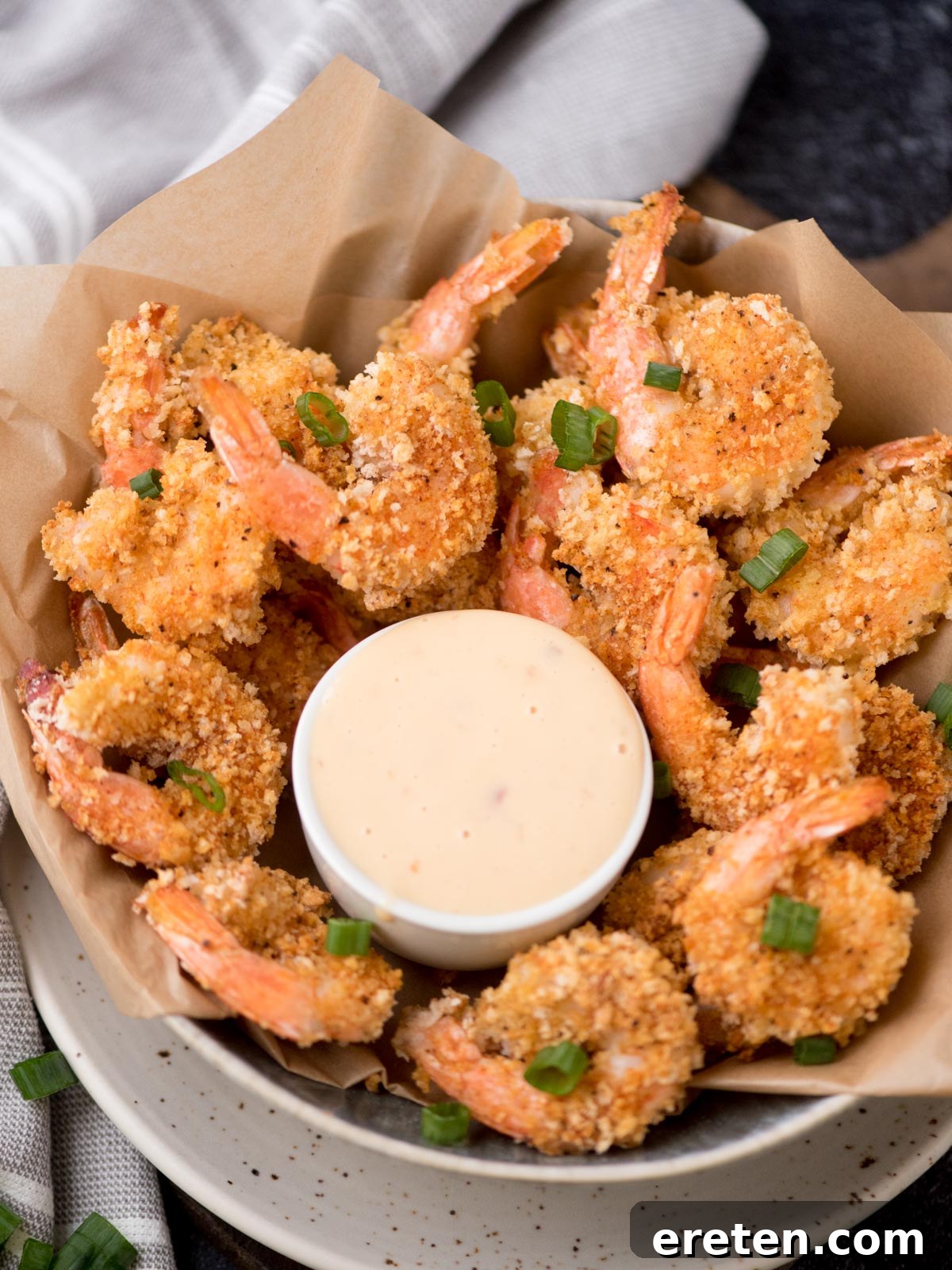 Crispy Baked Bang Bang Shrimp 2 A bowl of vibrant Bang Bang Shrimp, garnished with fresh green onions, ready to be enjoyed. A small white bowl of the signature sauce sits alongside.