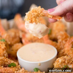 Crispy Baked Bang Bang Shrimp 8 crispy shrimp being dipped in bang bang sauce in a small bowl